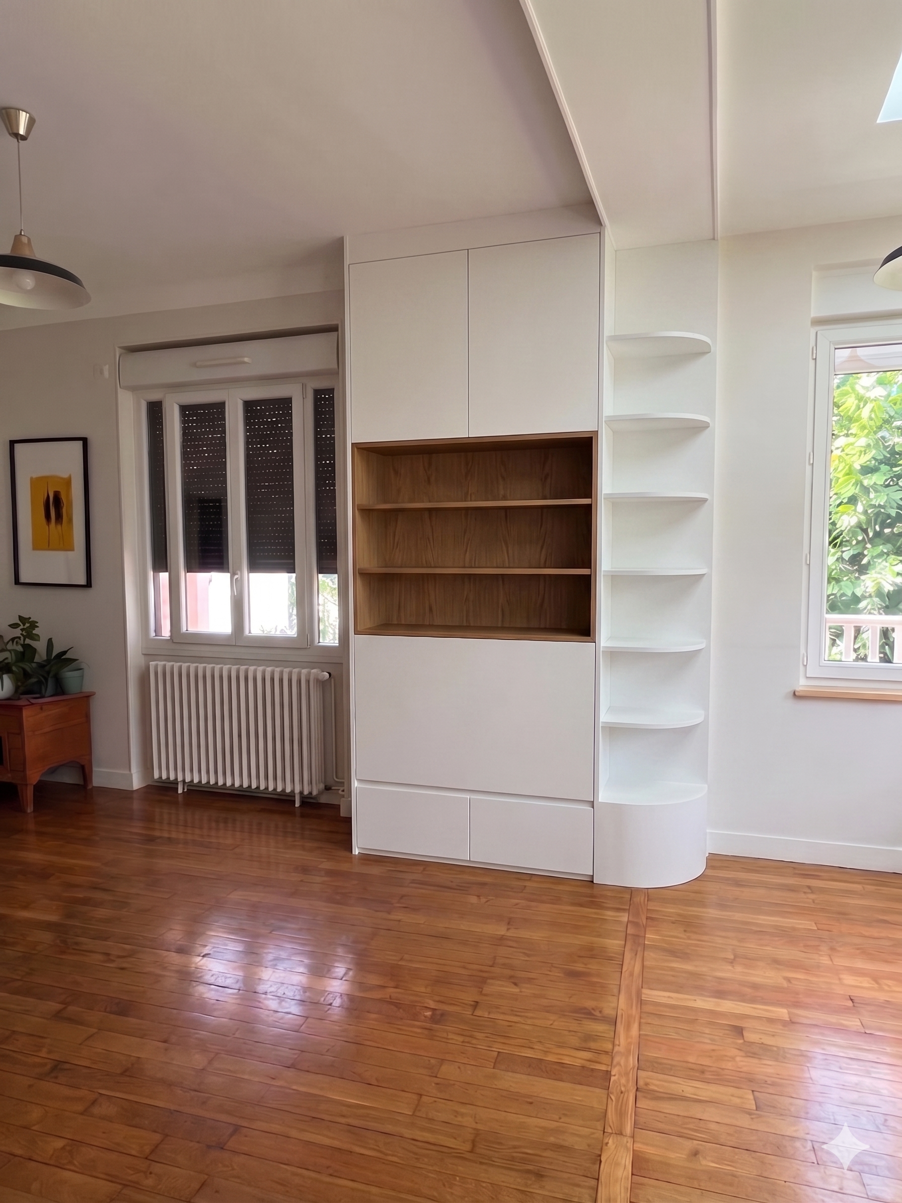 Une pièce avec un parquet en bois clair, une fenêtre ouverte laissant entrer la lumière, un radiateur, et une étagère blanche intégrée dans un mur blanc, avec un tableau dans le coin gauche.