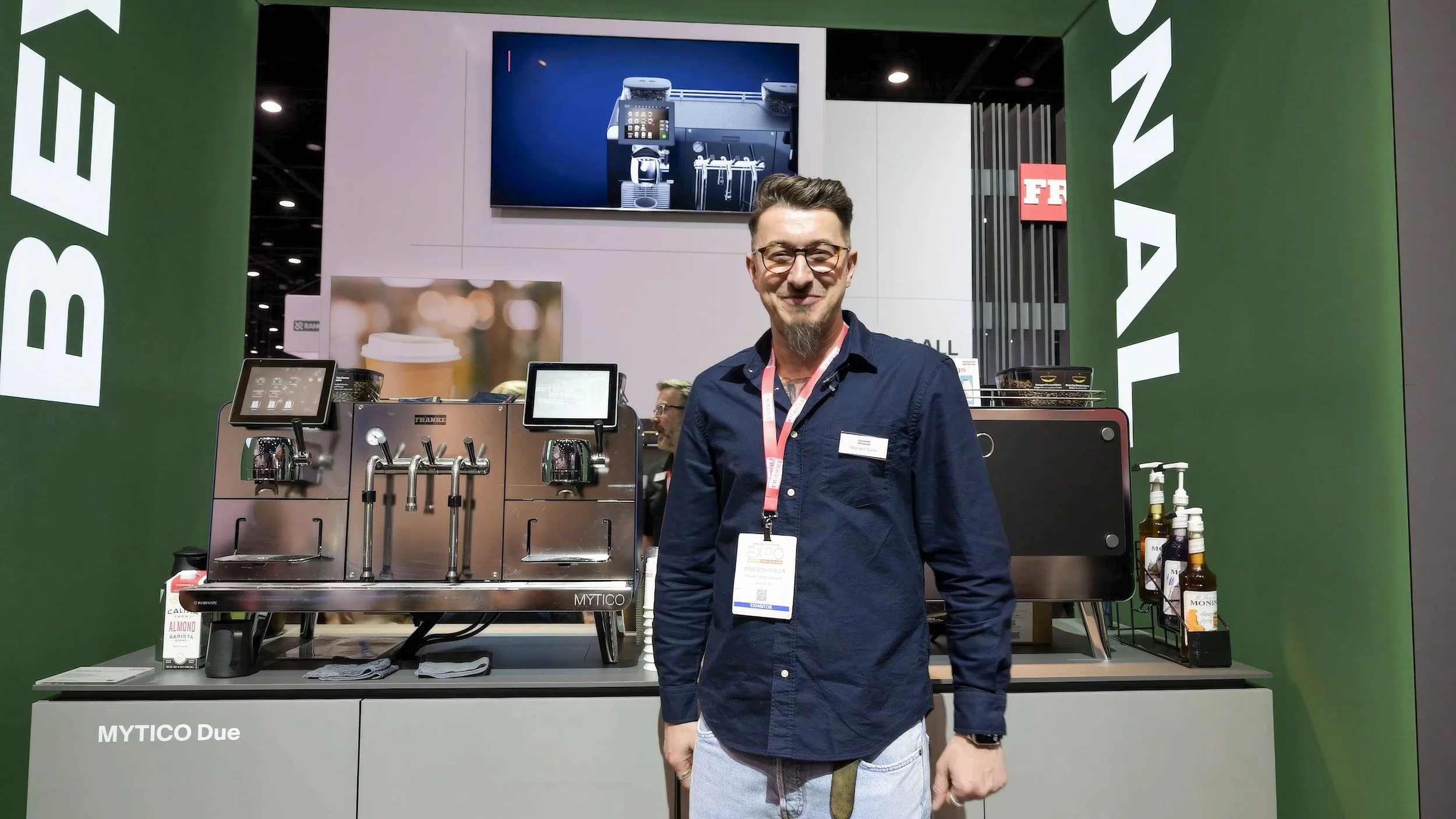 Man infront of trade show table with fancy coffee machine.