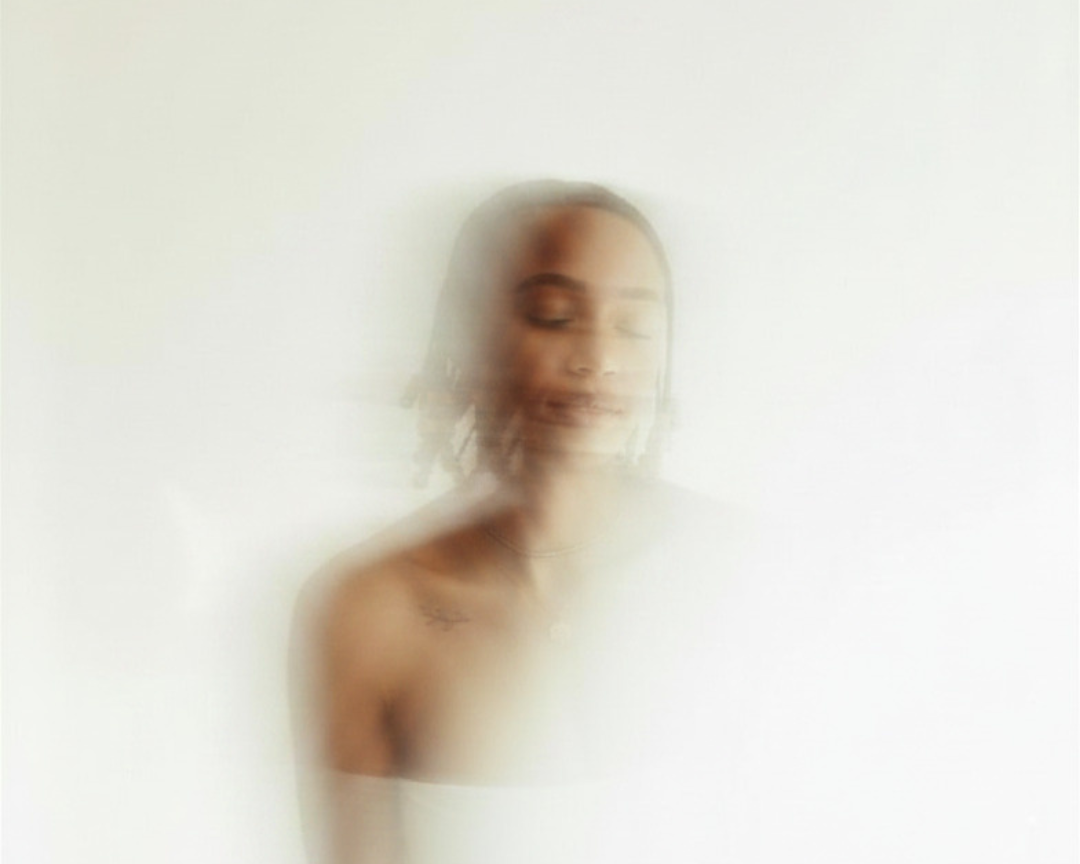 Blurred, hazy image of a dark-skinned woman with hair braids and eyes closed