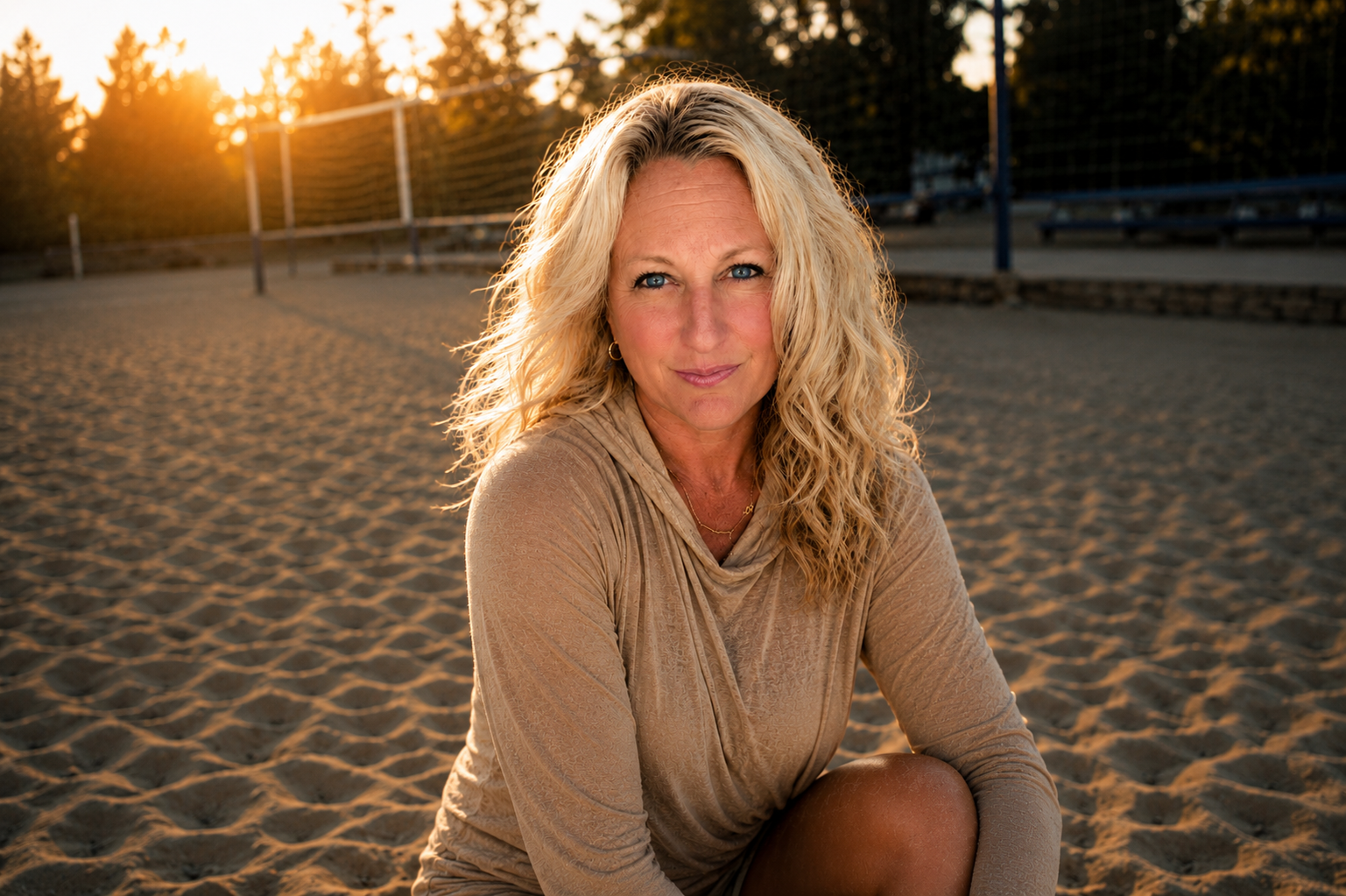 Woman sitting on a sand volleyball court after playing at golden hour.