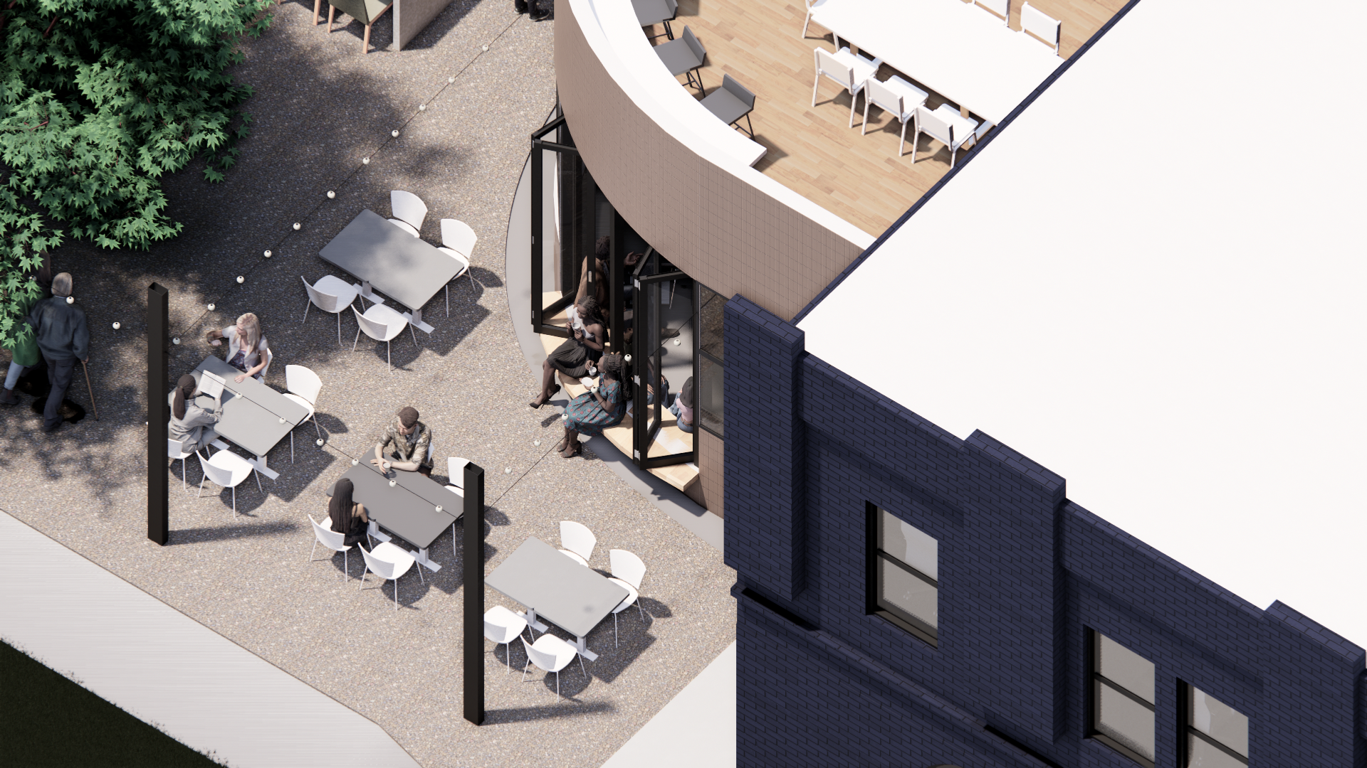 Outdoor seating area with tables and chairs on a gravel surface, adjacent to a modern building with large glass windows and a corner outdoor cafe or lounge space with people sitting and chatting.