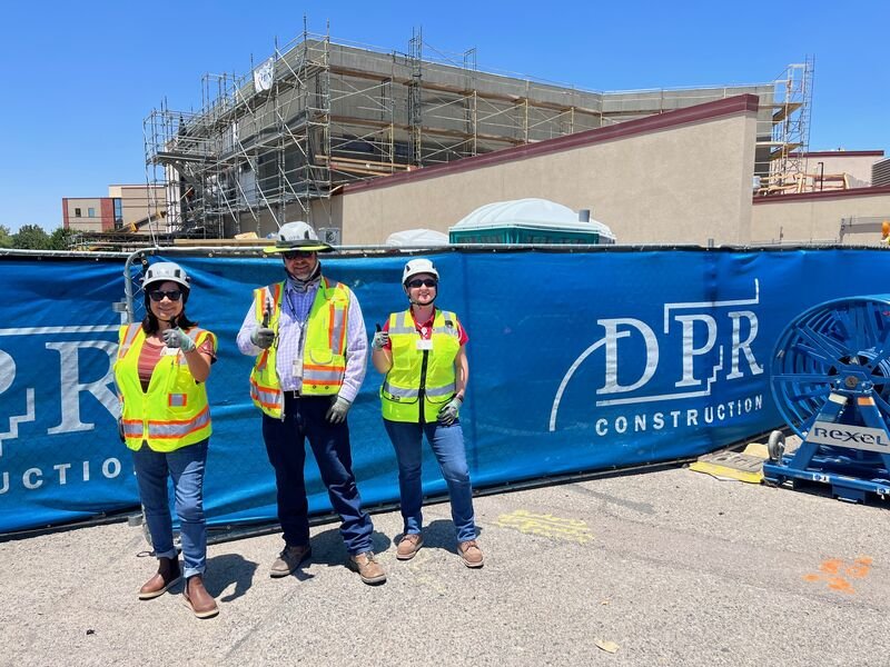 Three workers in front of a DPR Construction fence wrap.