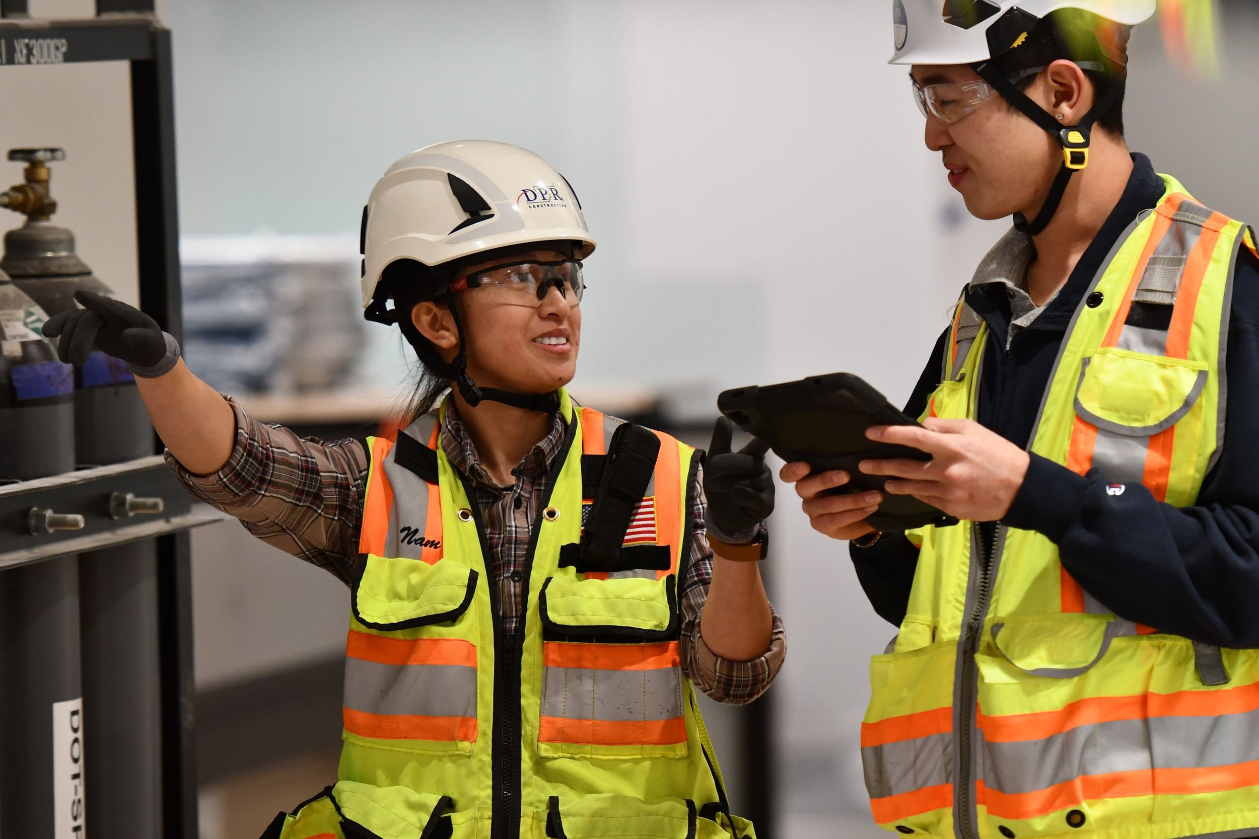 Two workers discuss plans on a jobsite while wearing PPE