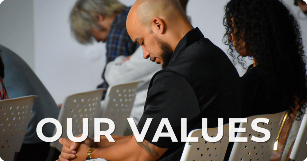 People attending a gathering or seminar, praying with heads bowed and hands clasped, with the text 'OUR VALUES' overlaid.