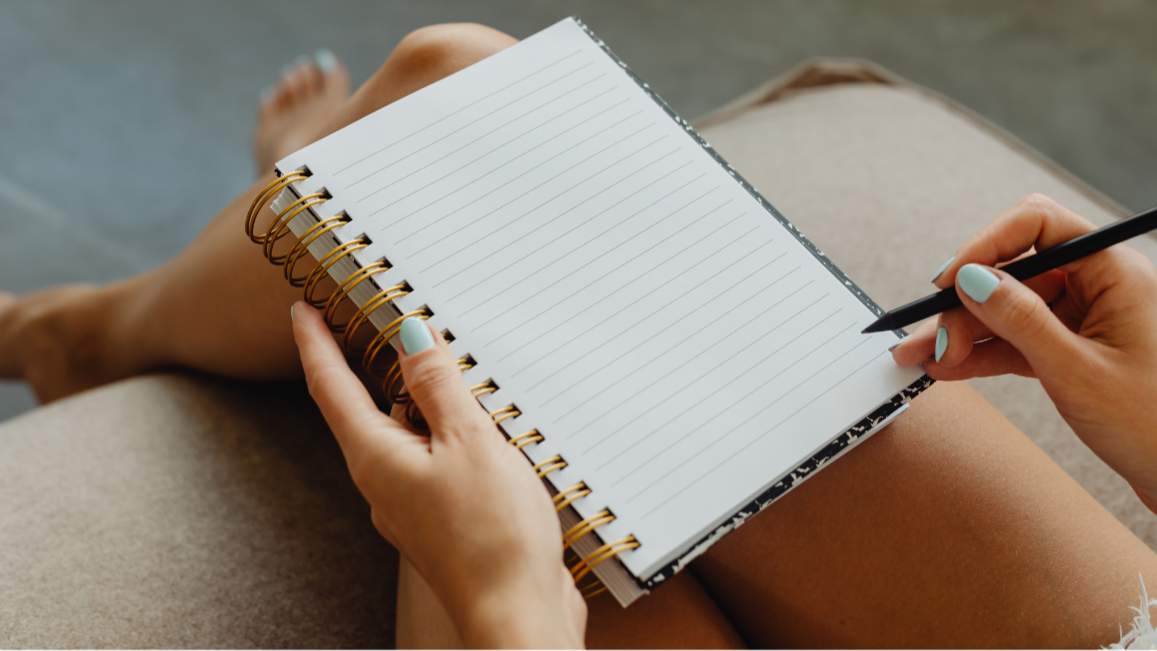 Image of a open, blank journal sitting on a woman's lap.  She holds a pen in her right hand.