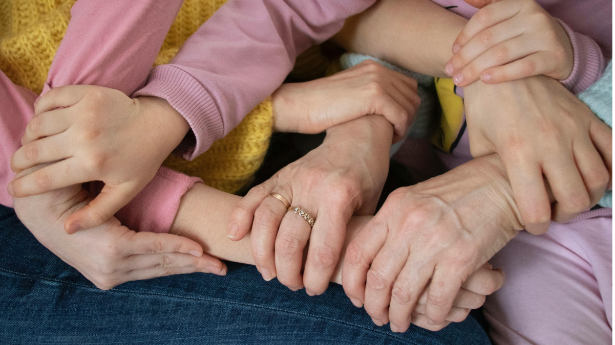Close-up of a parent and children sitting together with their hands gently holding each other’s arms, symbolizing family support and connection.