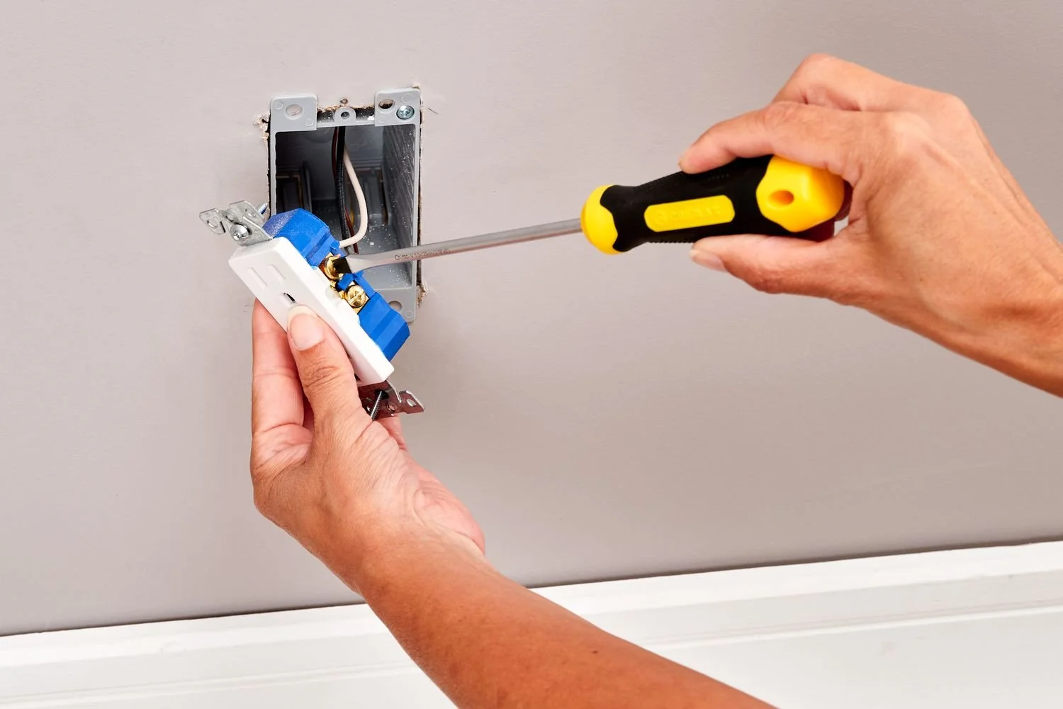 Person installing or repairing an electrical outlet or switch in a wall using a screwdriver.