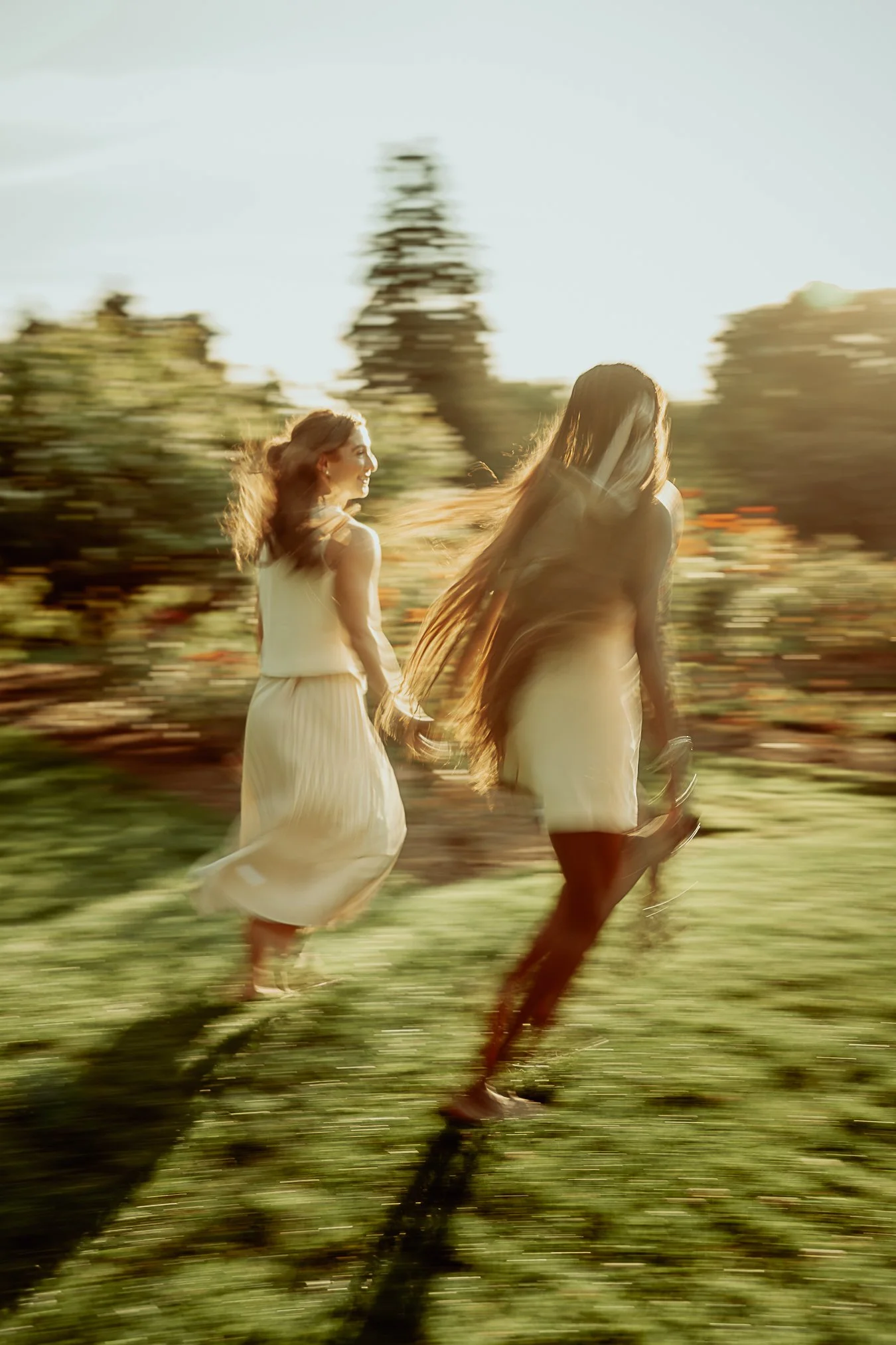 Two women running outdoors at sunset, blurred motion with warm lighting and greenery in the background.
