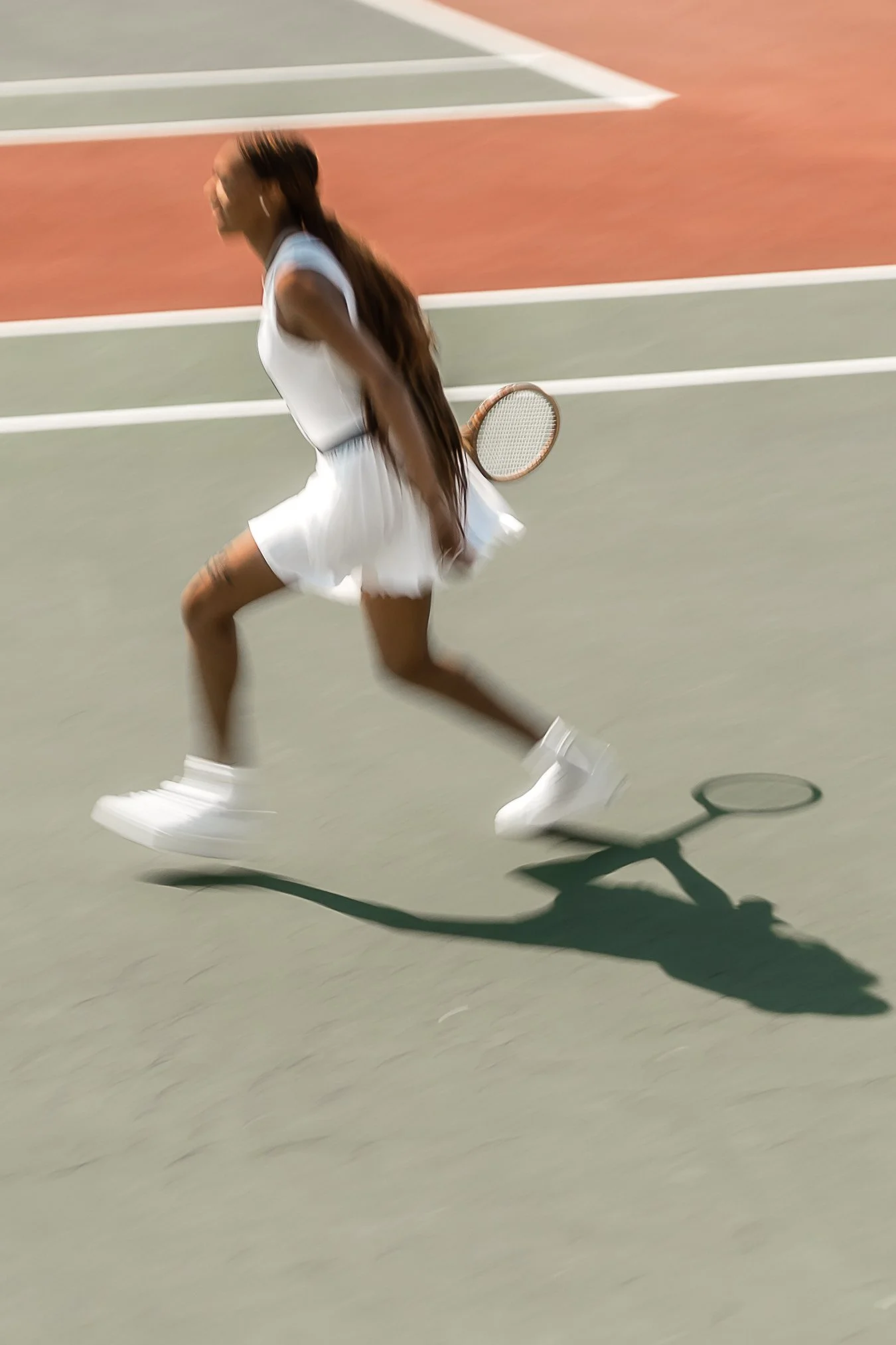 A woman running on a tennis court in a white dress holding a tennis racket.