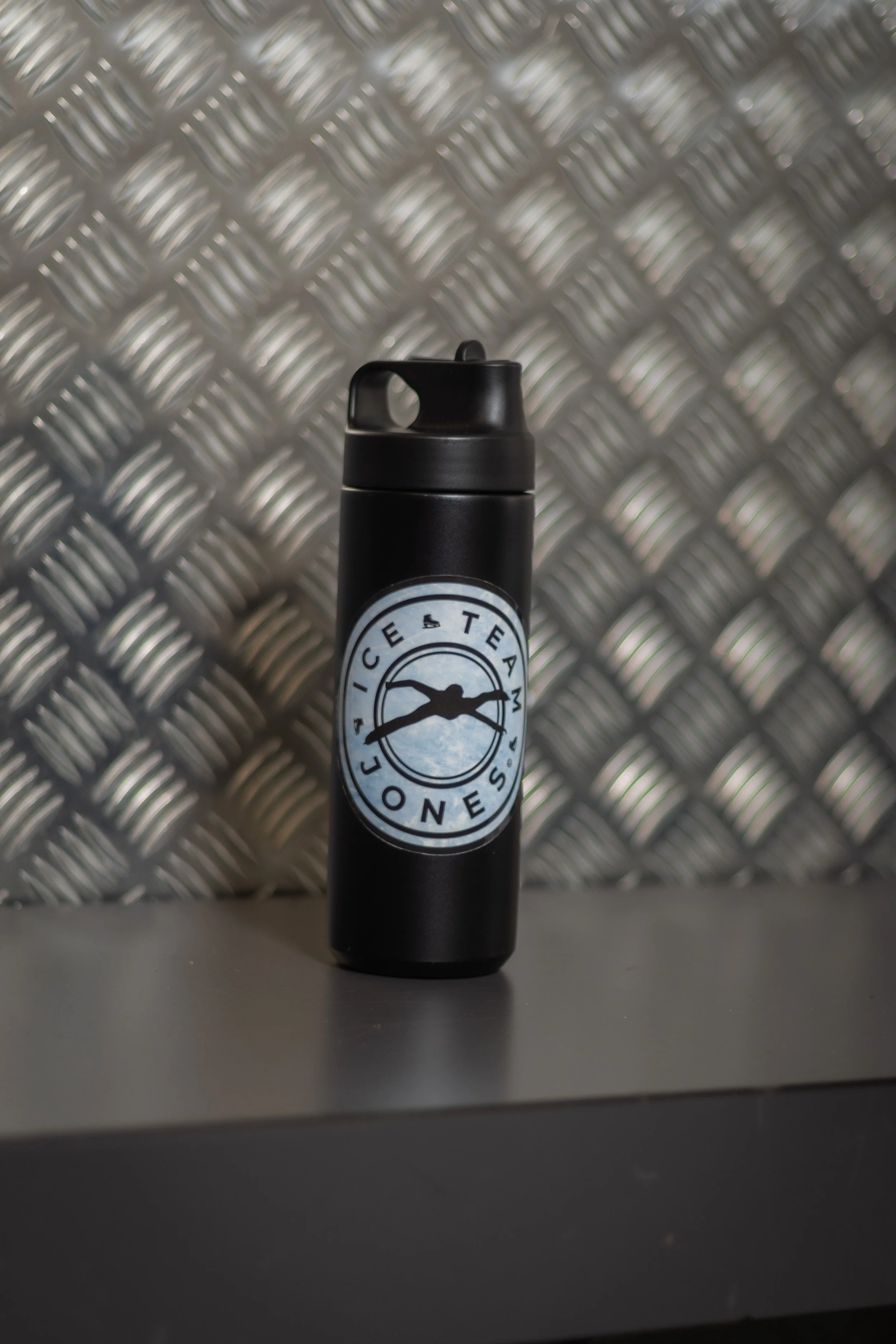 Black tumbler with a "Ice Team Jones" logo, placed on a gray surface against a metallic, diamond-plate wall.