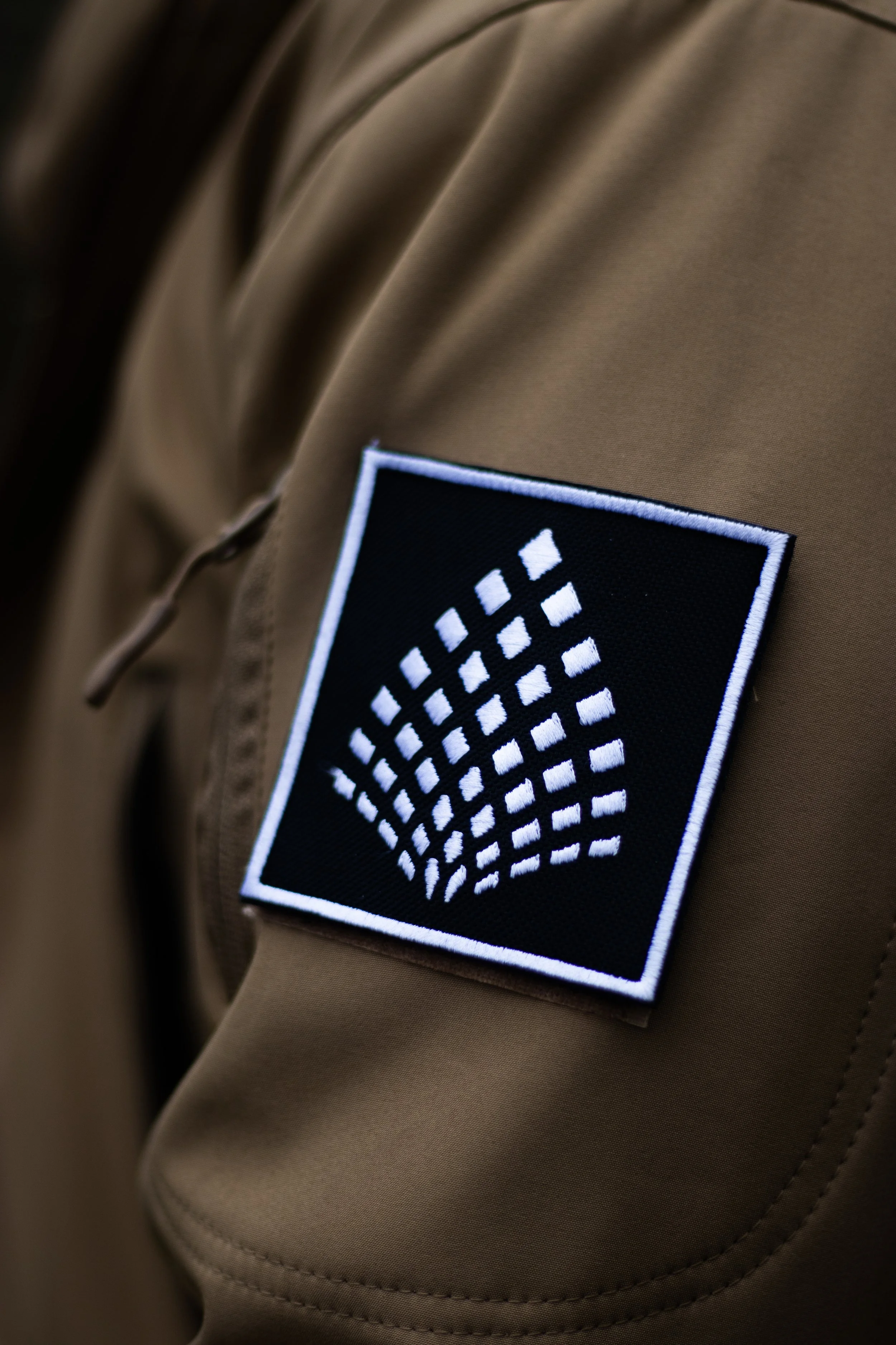 Close-up of a tan jacket with a black and white patch featuring a stylized tree design.