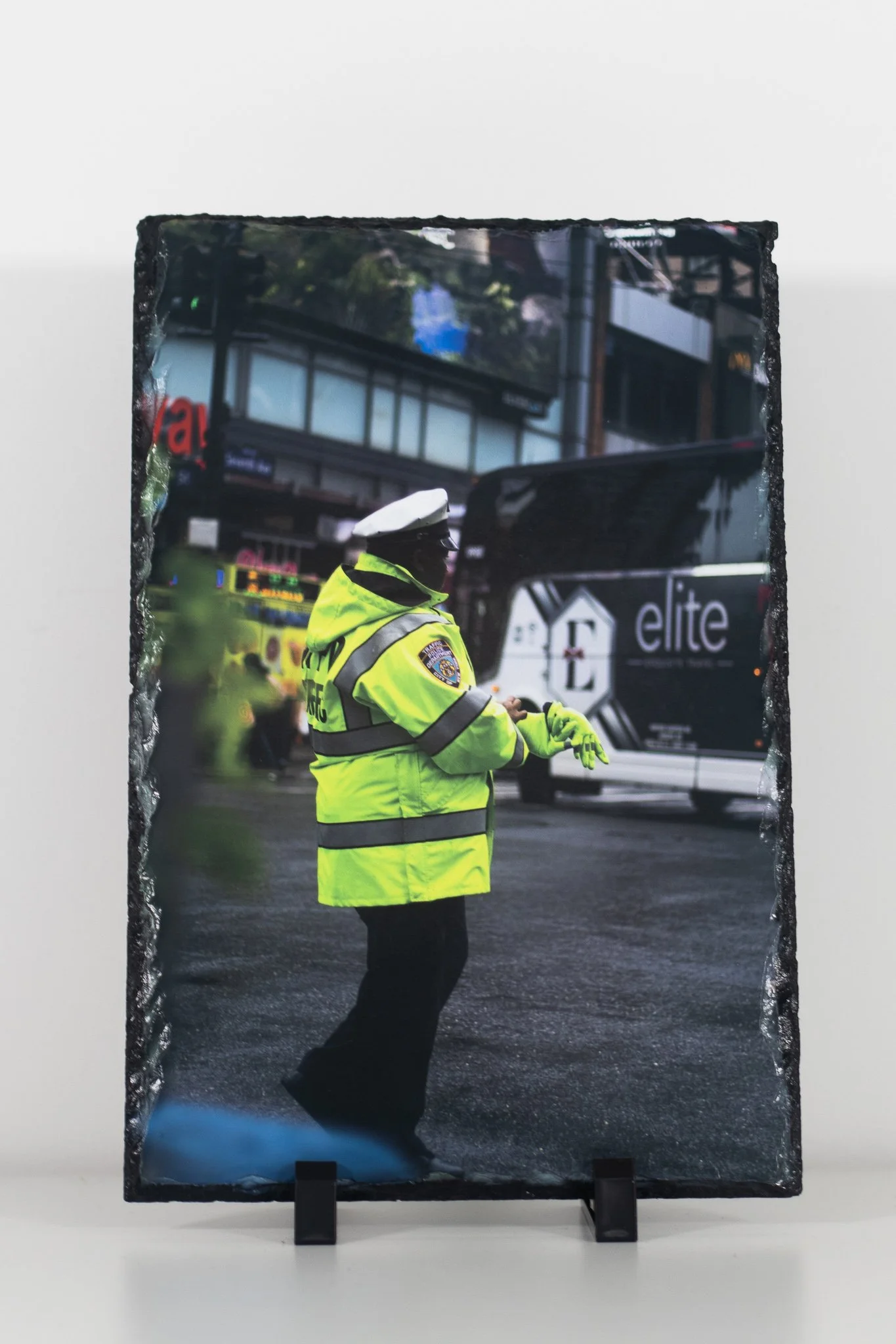 A person dressed as a police officer in a fluorescent yellow jacket and white cap standing on a city street, with a bus and buildings in the background.