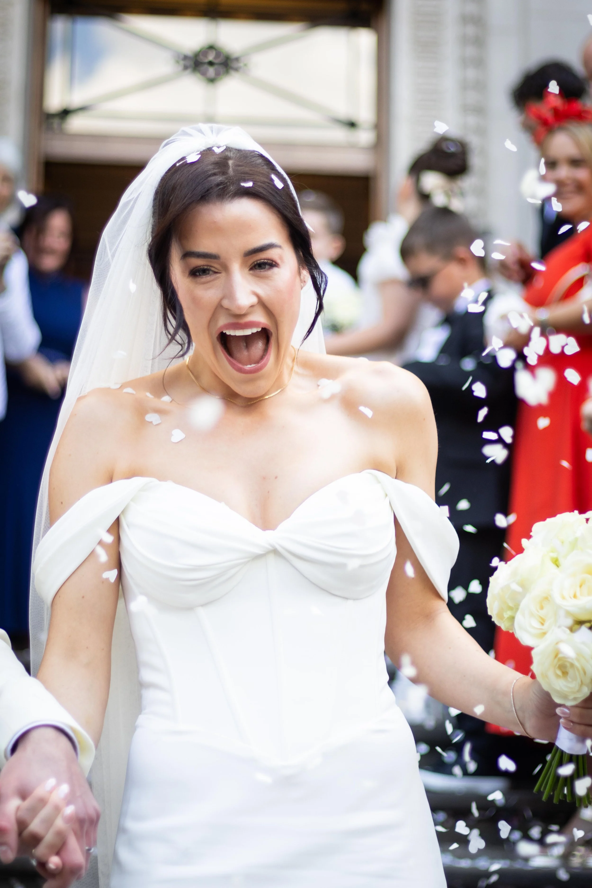 A bride in a white wedding dress and veil celebrating with confetti at her wedding reception.