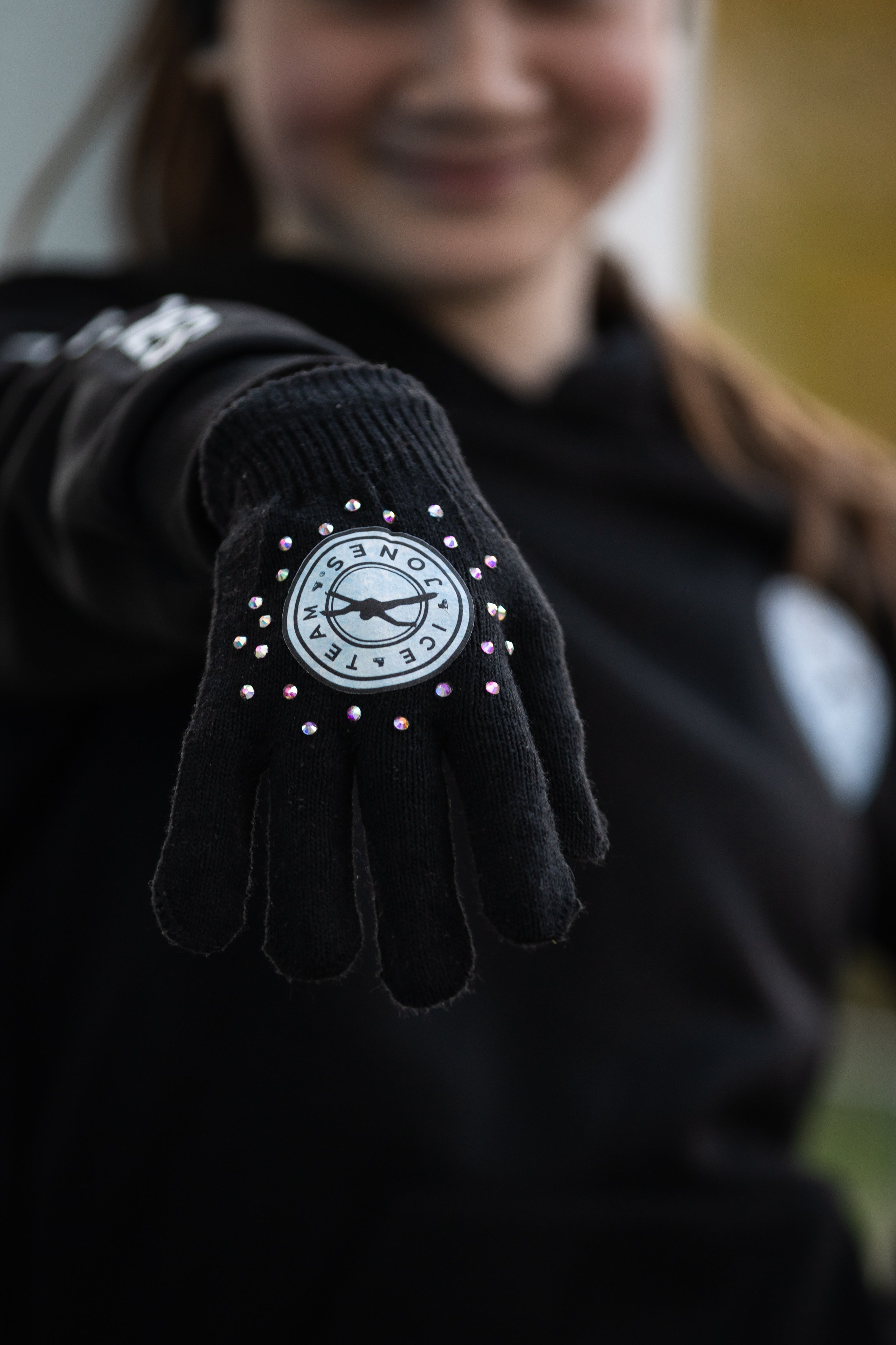 A person wearing a black glove with rhinestones and a logo, smiling and showing their hand.