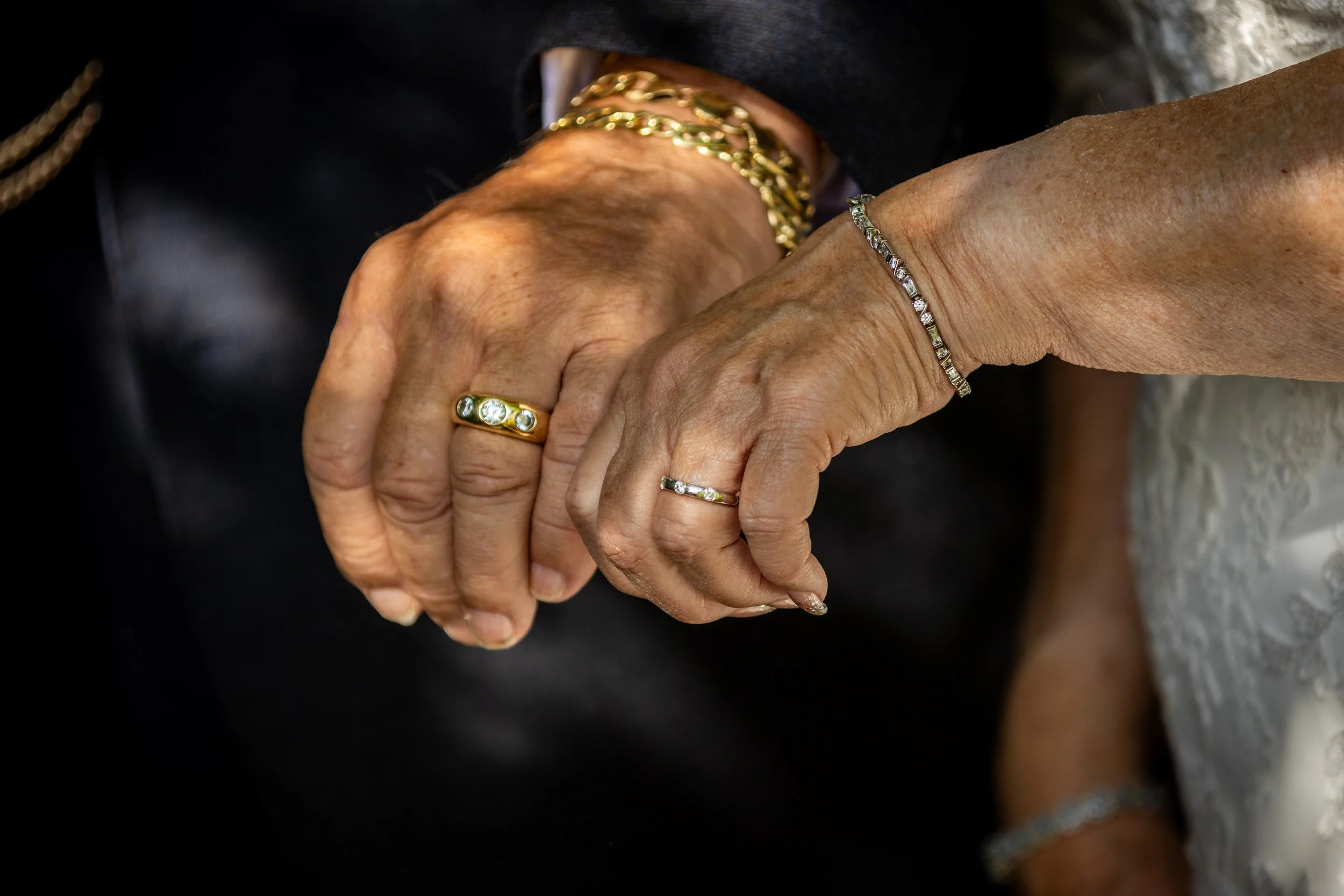Close-up of elderly hands holding each other, adorned with rings, bracelets, and gold jewelry.