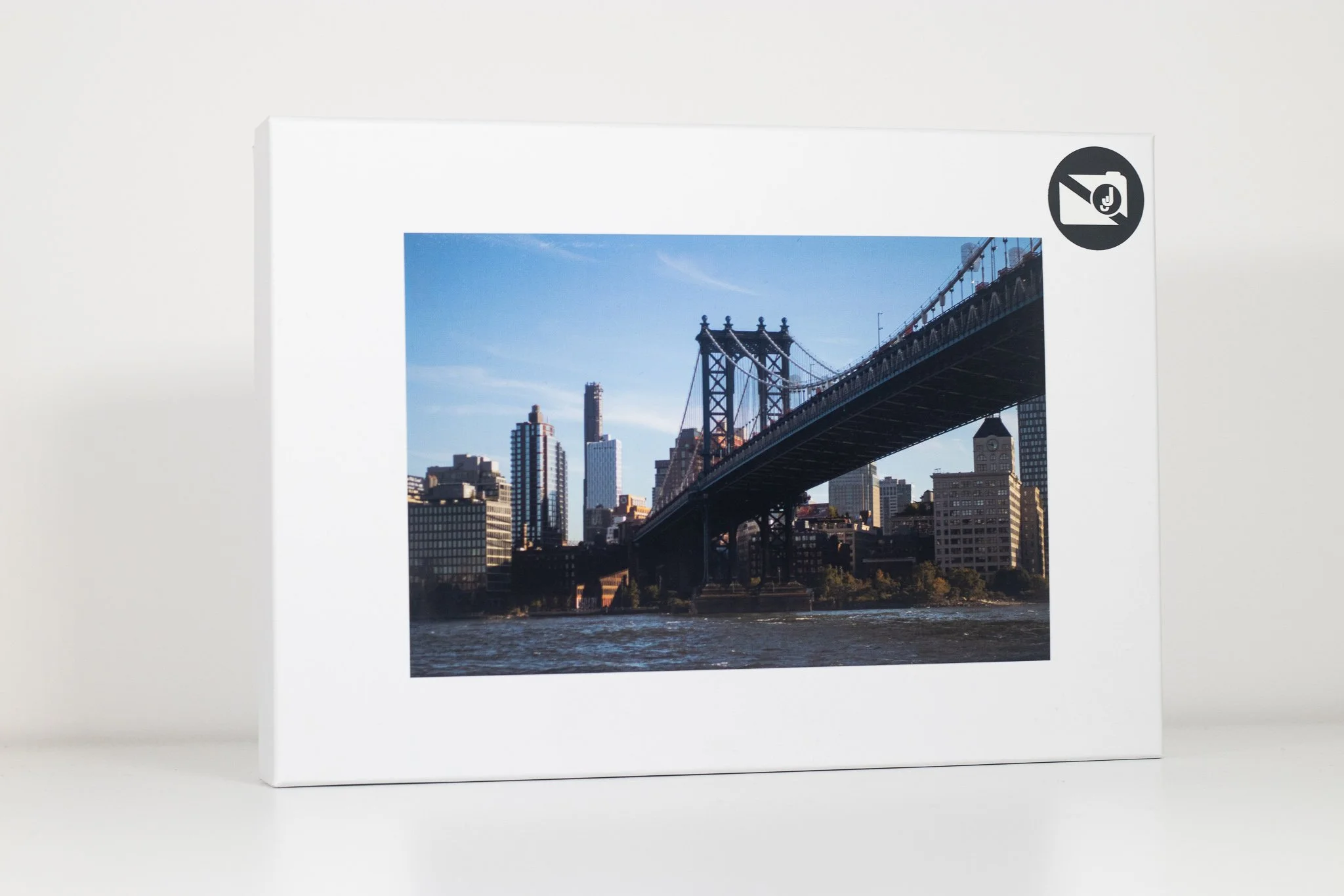 Photo of a city skyline with a suspension bridge over water, some tall buildings and a clear blue sky.