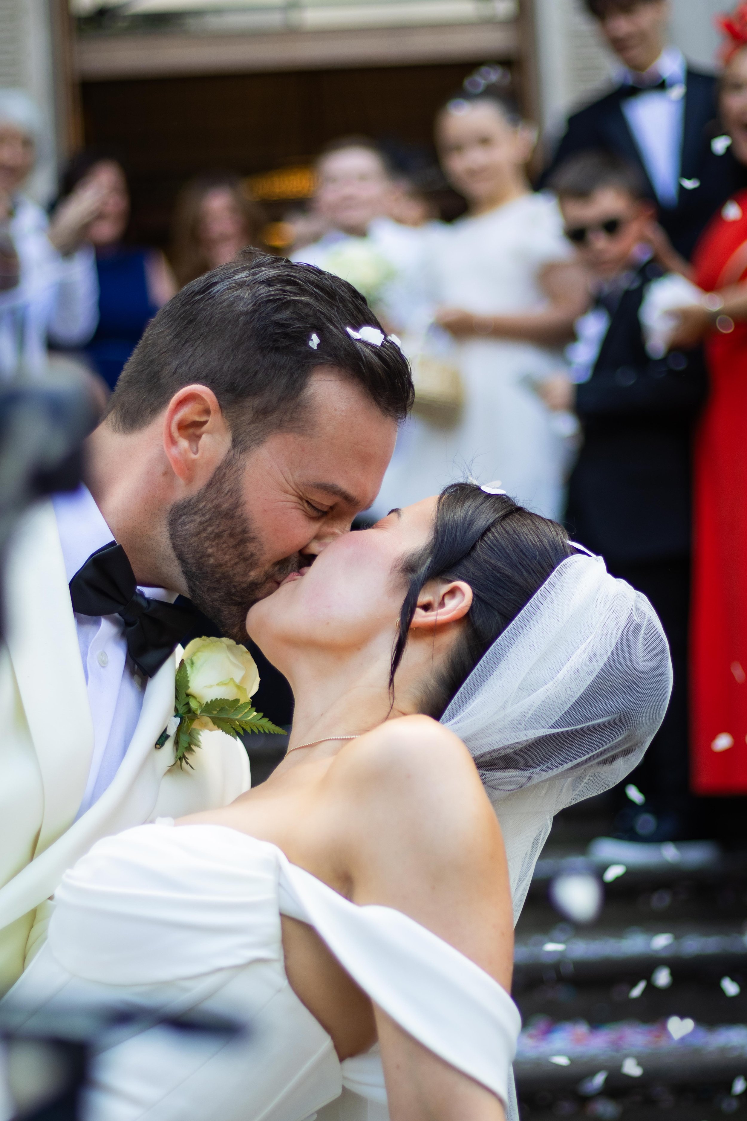 A bride and groom kiss during their wedding, surrounded by friends and family.