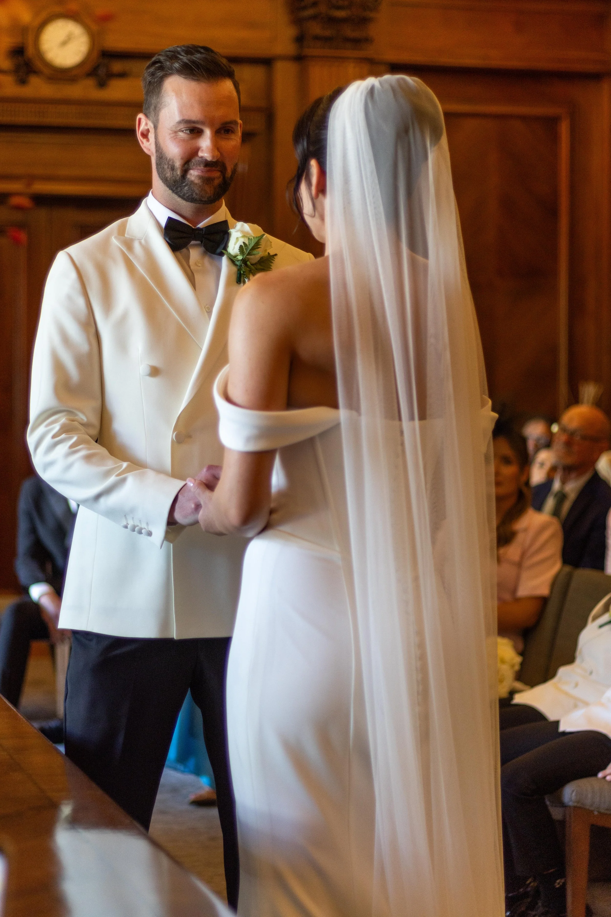 A bride and groom exchange vows during a wedding ceremony in a wood-paneled room.