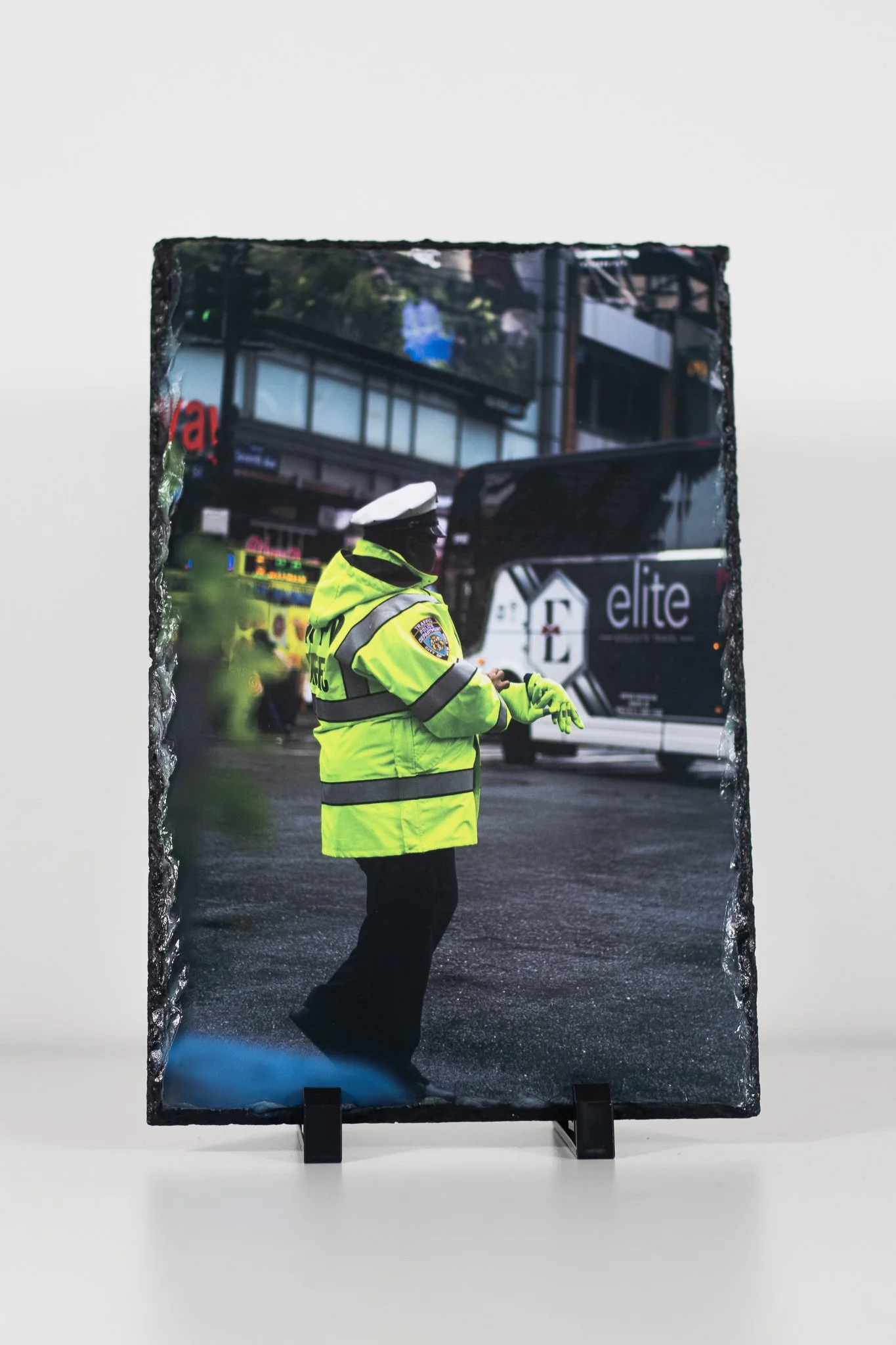 A police officer in a high-visibility yellow jacket and cap in a city street, with buses and buildings in the background.