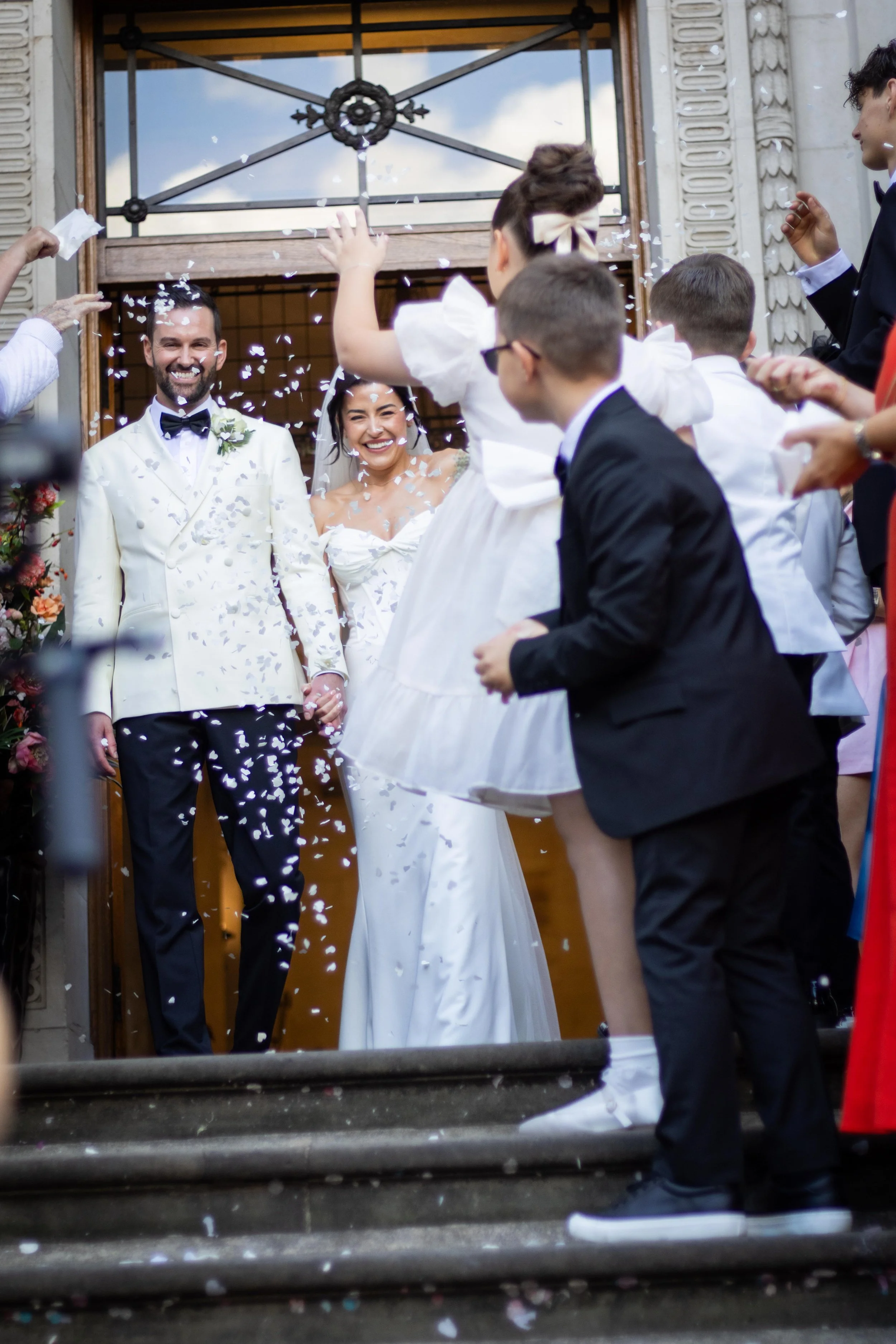 Bride and groom standing at the entrance, smiling, as guests throw confetti on their wedding day.