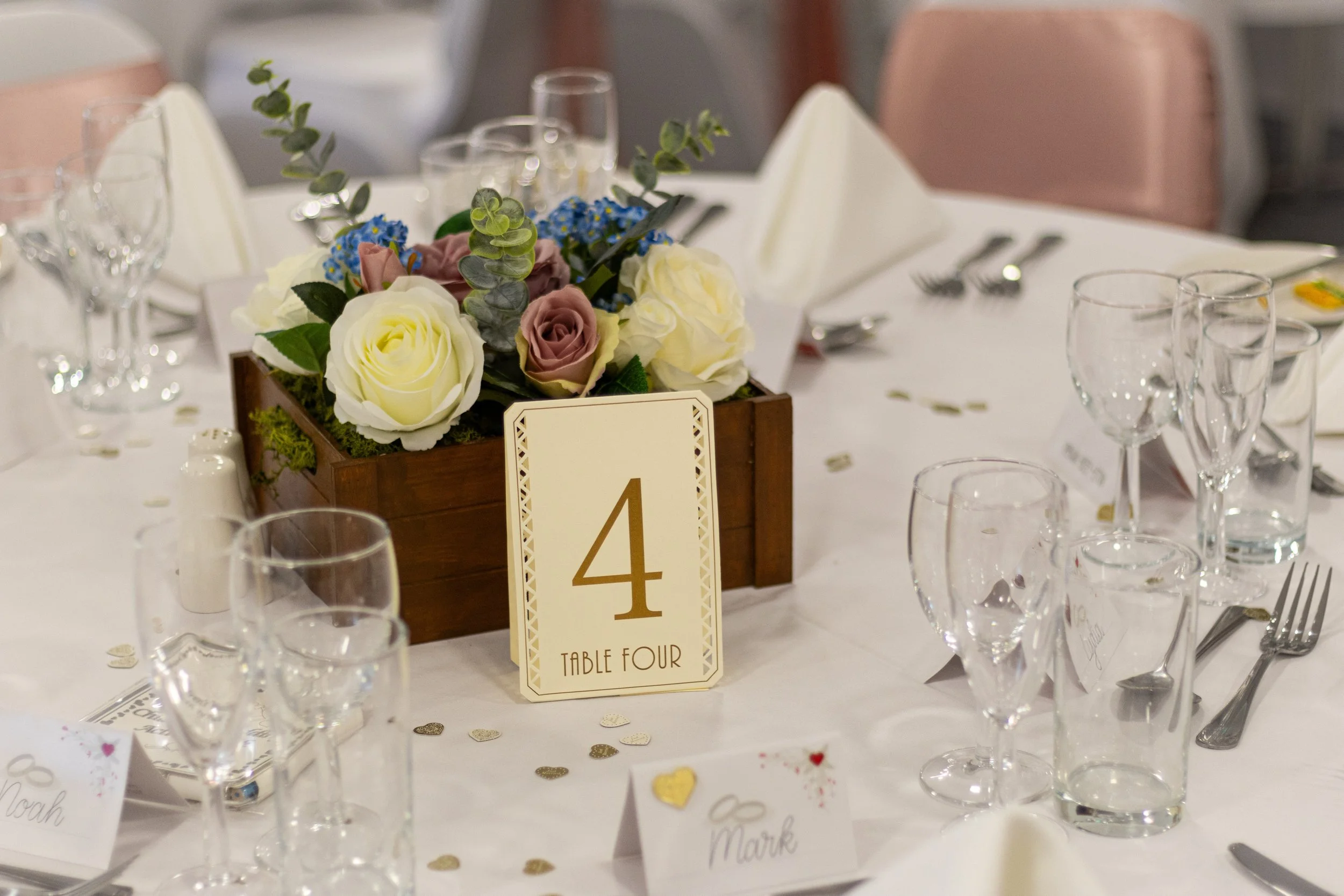 Wedding reception table with a flower centerpiece, table number 4, and place cards.