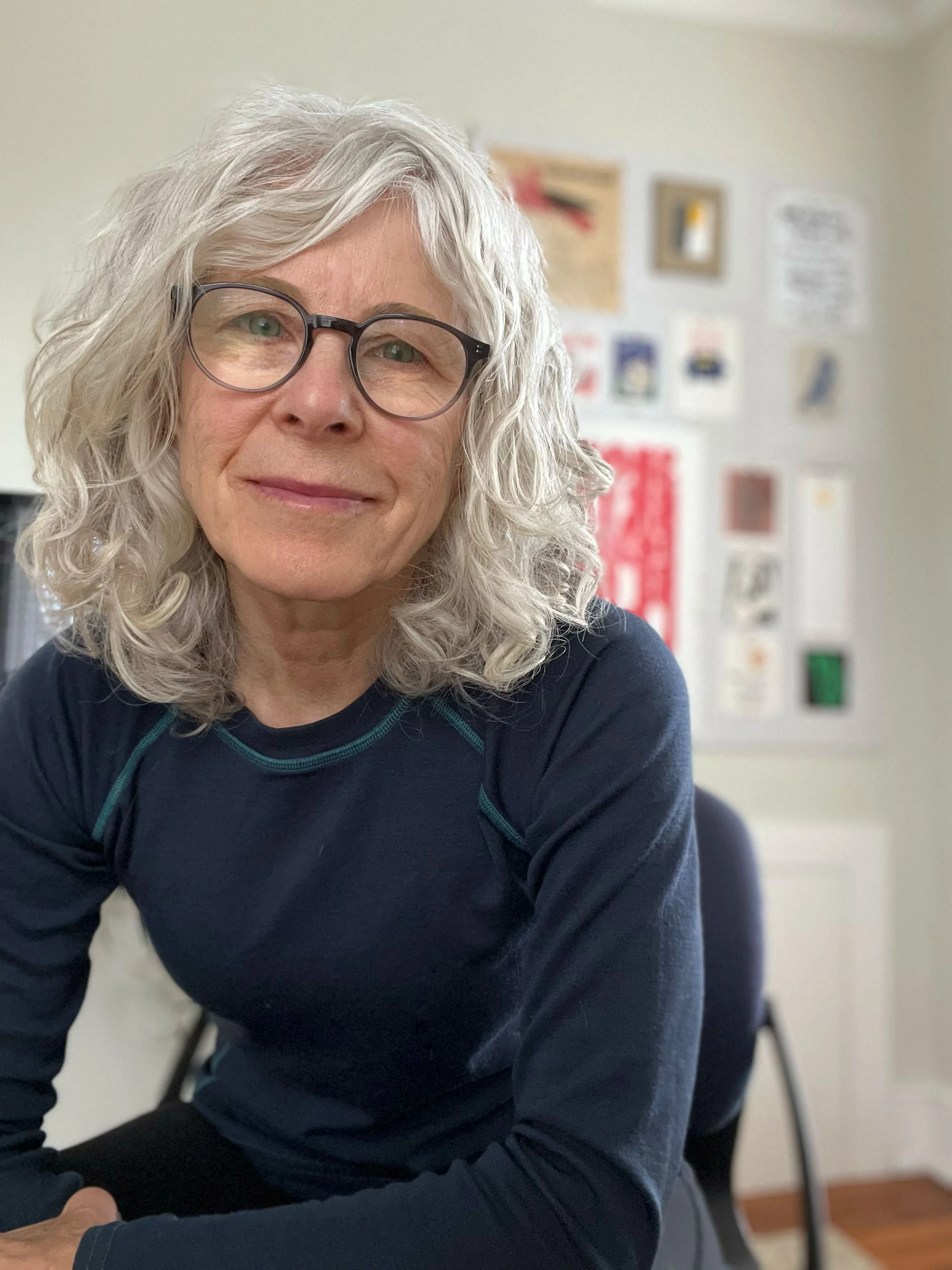 Adrienne DiGiovine sitting in her studio with details of various pieces of art in the background.