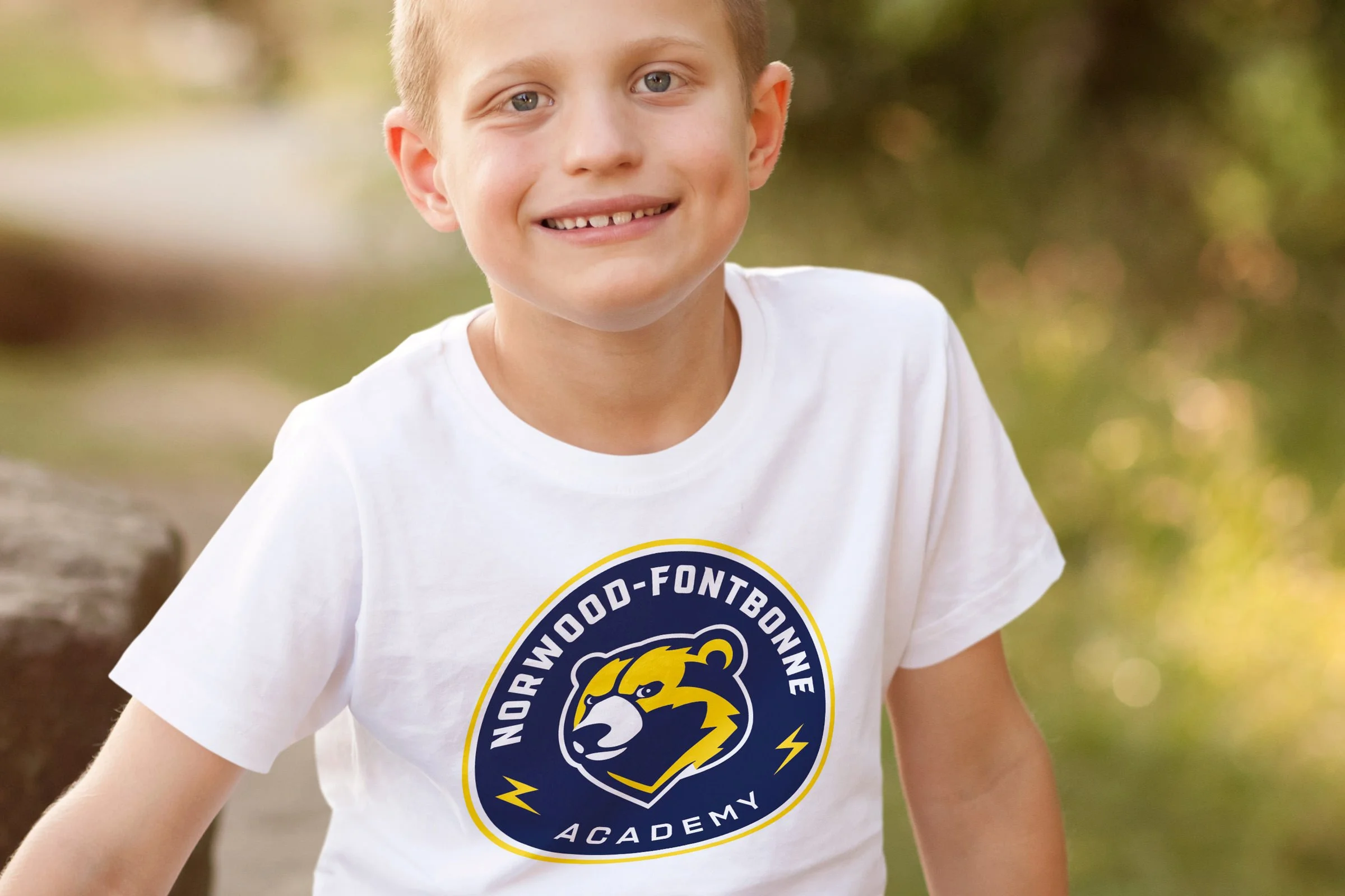 Young boy wearing a white t-shirt with circular Norwood-Fontbonne Academy athletic logo.