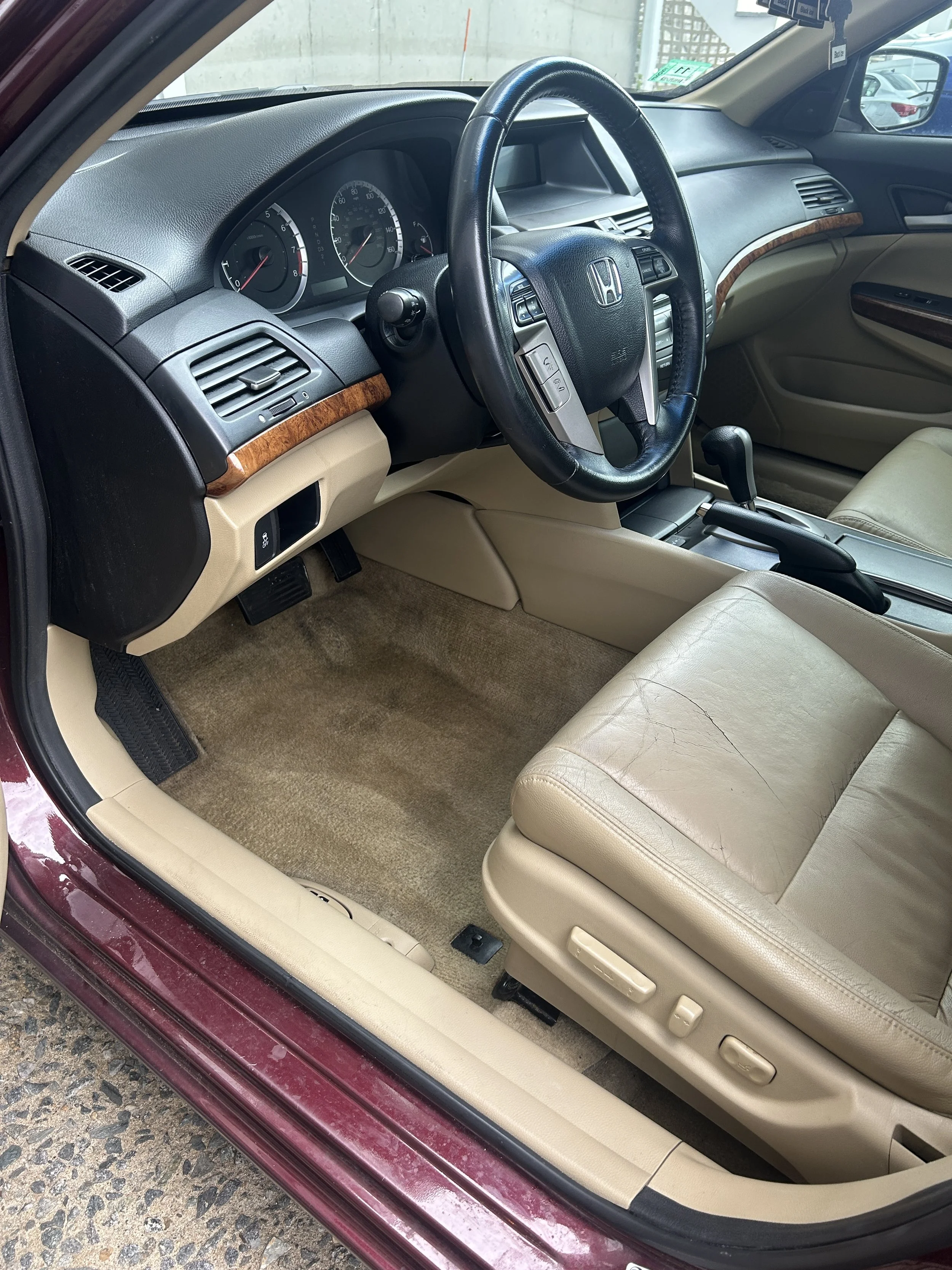 The interior of a Honda vehicle showing the driver's seat, steering wheel, dashboard with gauges, gear shift, and beige leather seats.