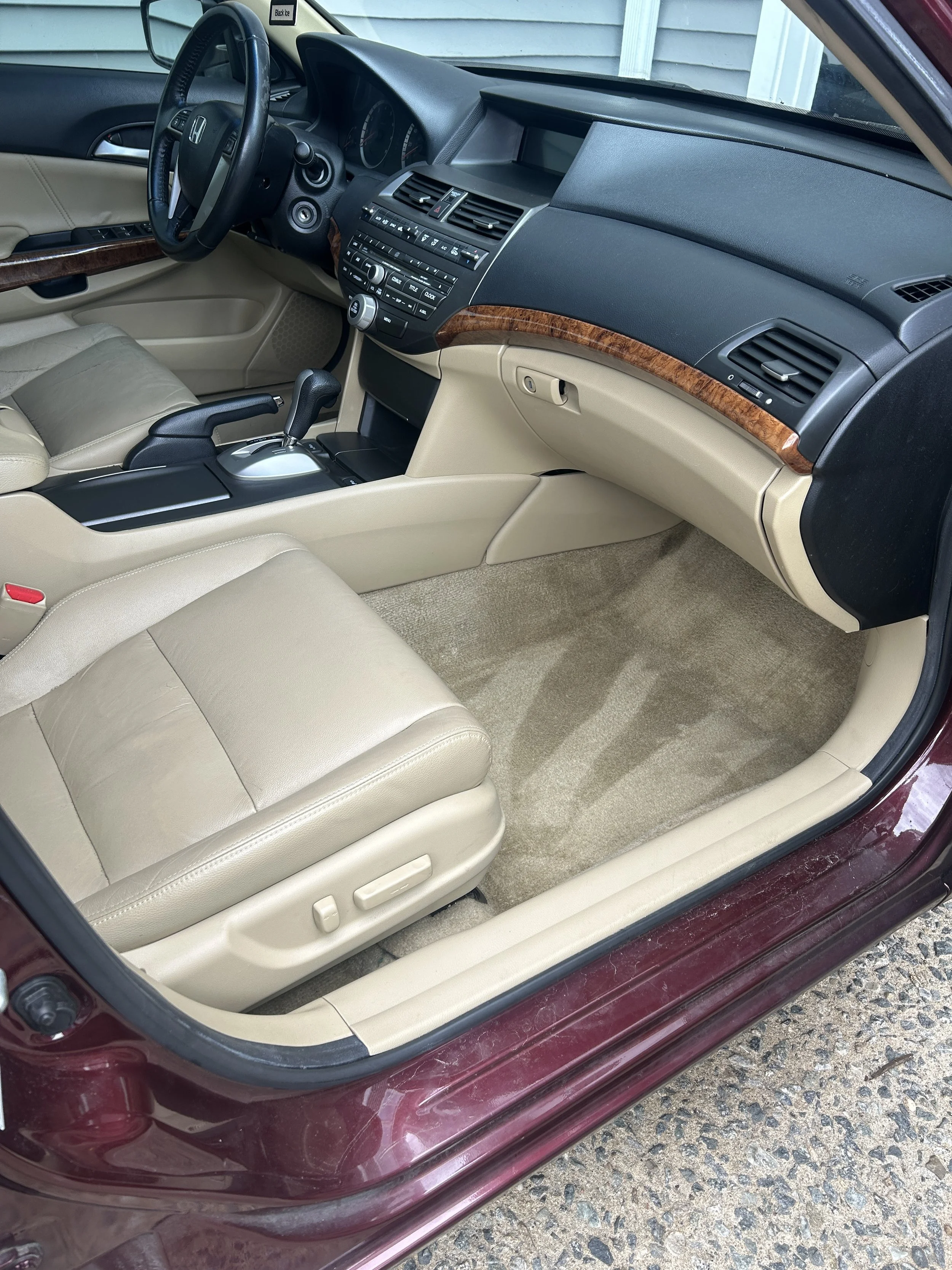 The interior of a beige Honda car showing the front passenger seat, dashboard, steering wheel, center console with gear shift, and part of the door with window controls.
