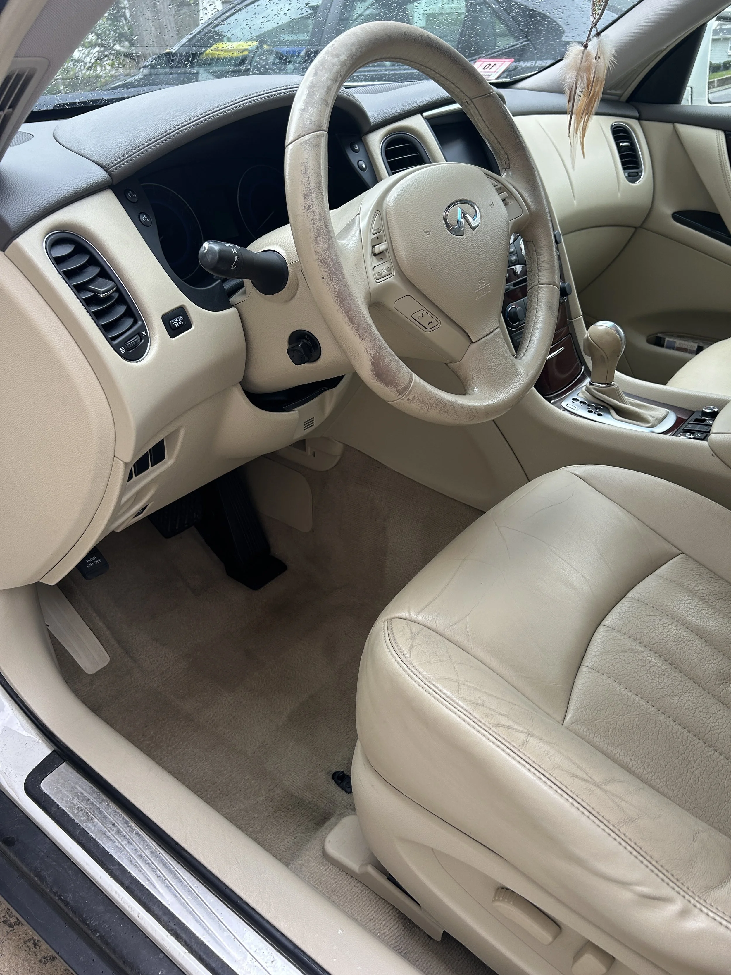 Interior of a beige luxury car showing the driver's seat, steering wheel, dashboard, and center console with gear shift.