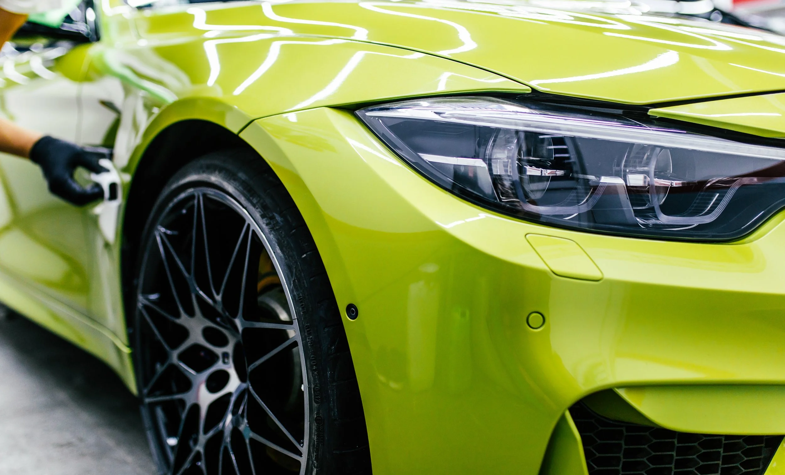 Close-up of a lime green sports car's front end, showing a sleek headlight, front wheel with intricate black alloy rim, and glossy body panels.