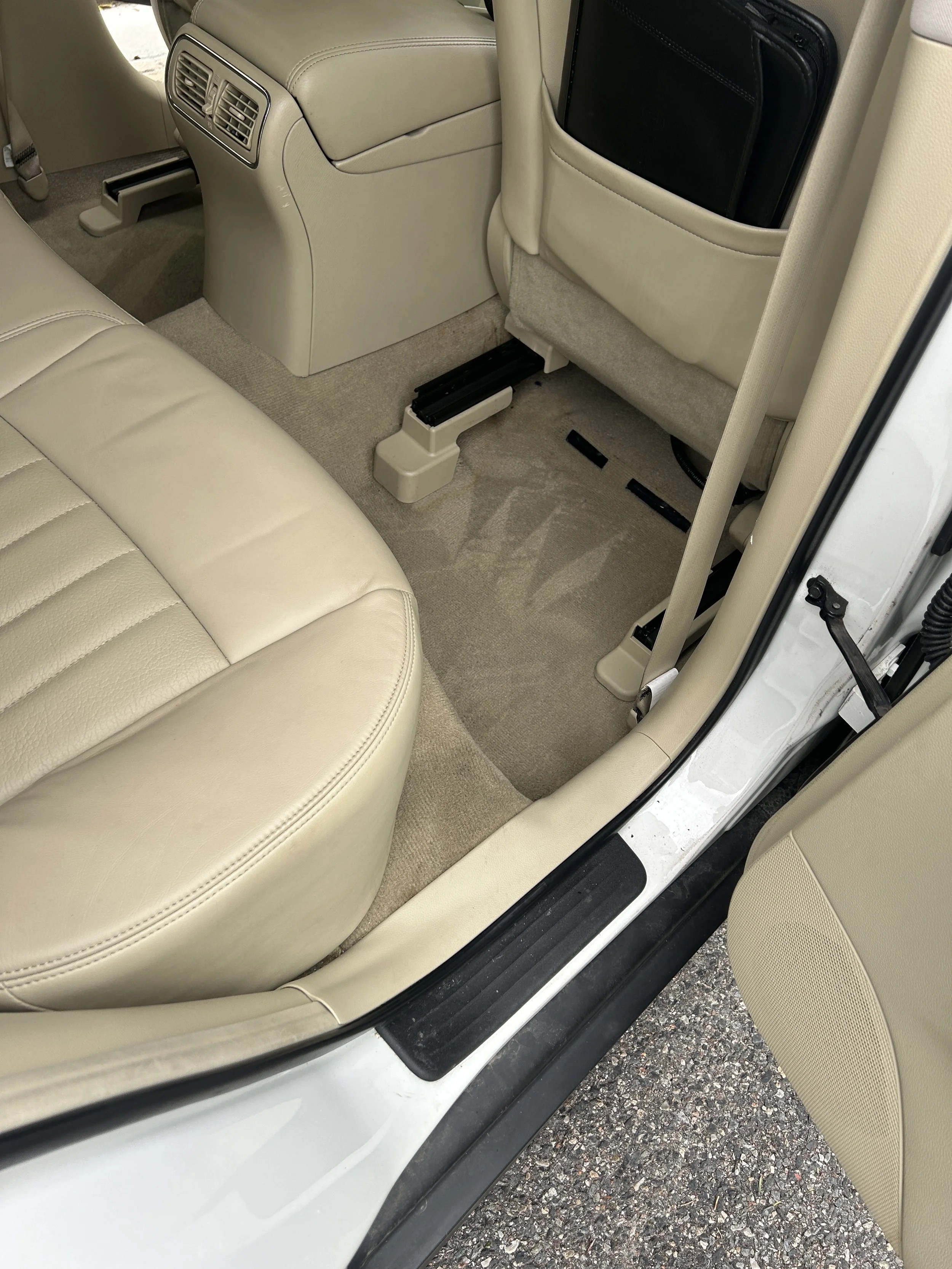 Interior of a car showing beige leather seats, beige carpet, and the back of the front passenger seat with a black document holder in a pocket.