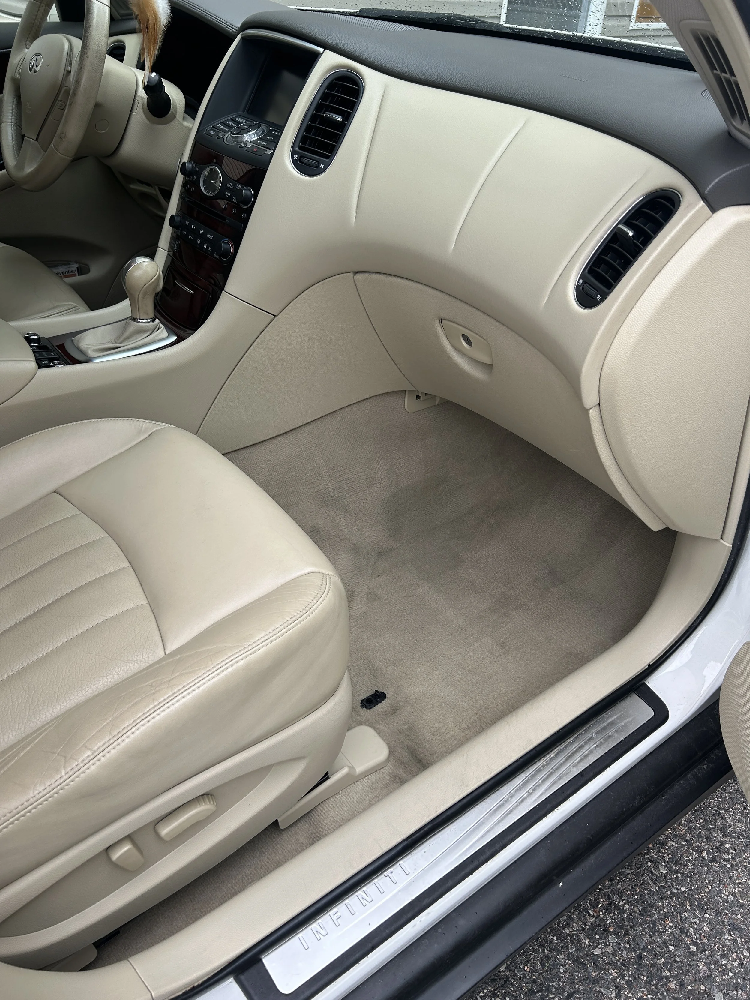 Interior of a beige Infiniti car showing the front passenger seat, dashboard, and center console.