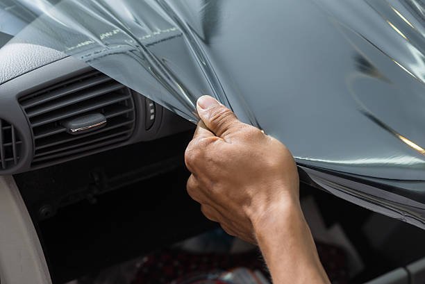 A person peeling off a protective film from a car's dashboard area.