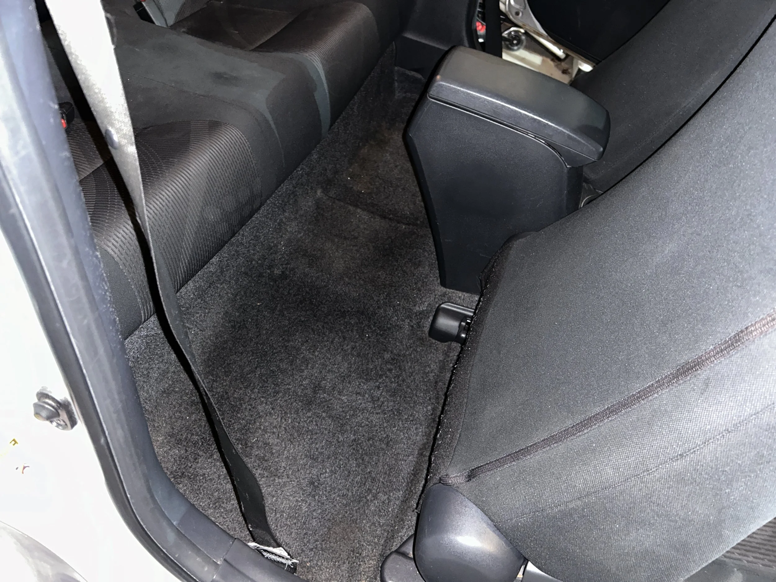 View of the back seat area of a car, showing dark fabric seats, floor, and the back of the front passenger seat.