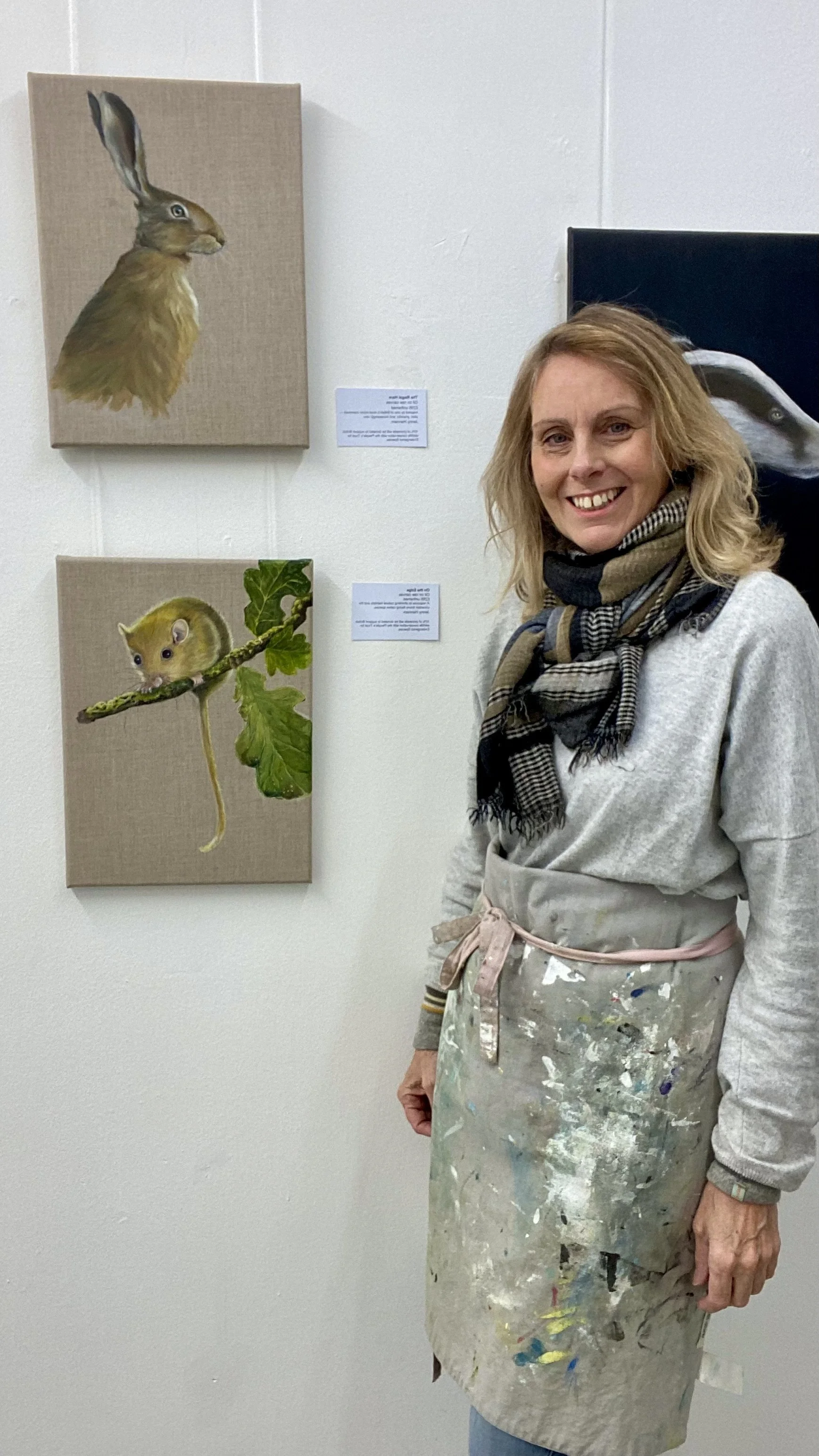 A woman standing in front of two paintings of animals, including a hare and a mouse, in an art gallery.