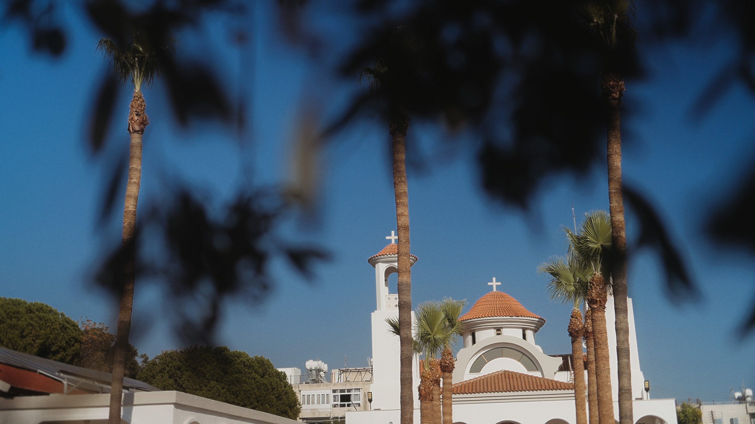 Greek Orthodox church exterior with palm trees and blue sky, Ayios Stylianos Church Agios Athanasios Cyprus, Red Lens Films