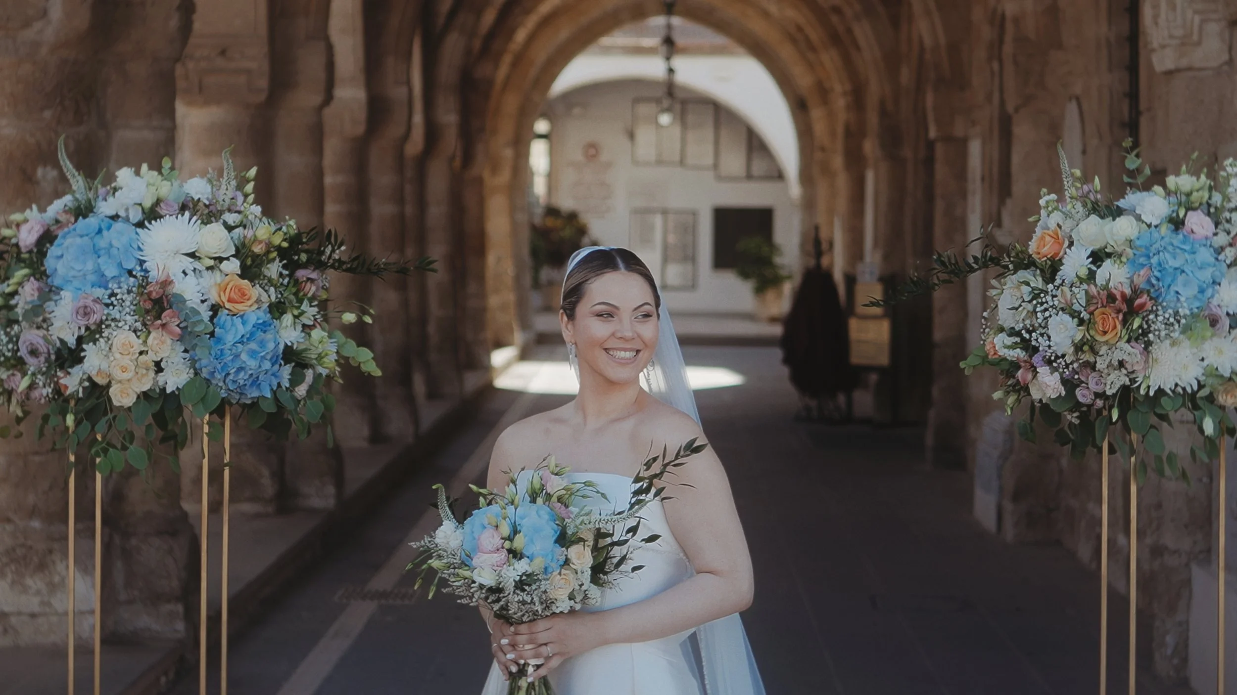 Bride Evgenia smiling with a blue hydrangea bouquet in the arcade of Saint Lazarus Church Larnaca, Red Lens Films