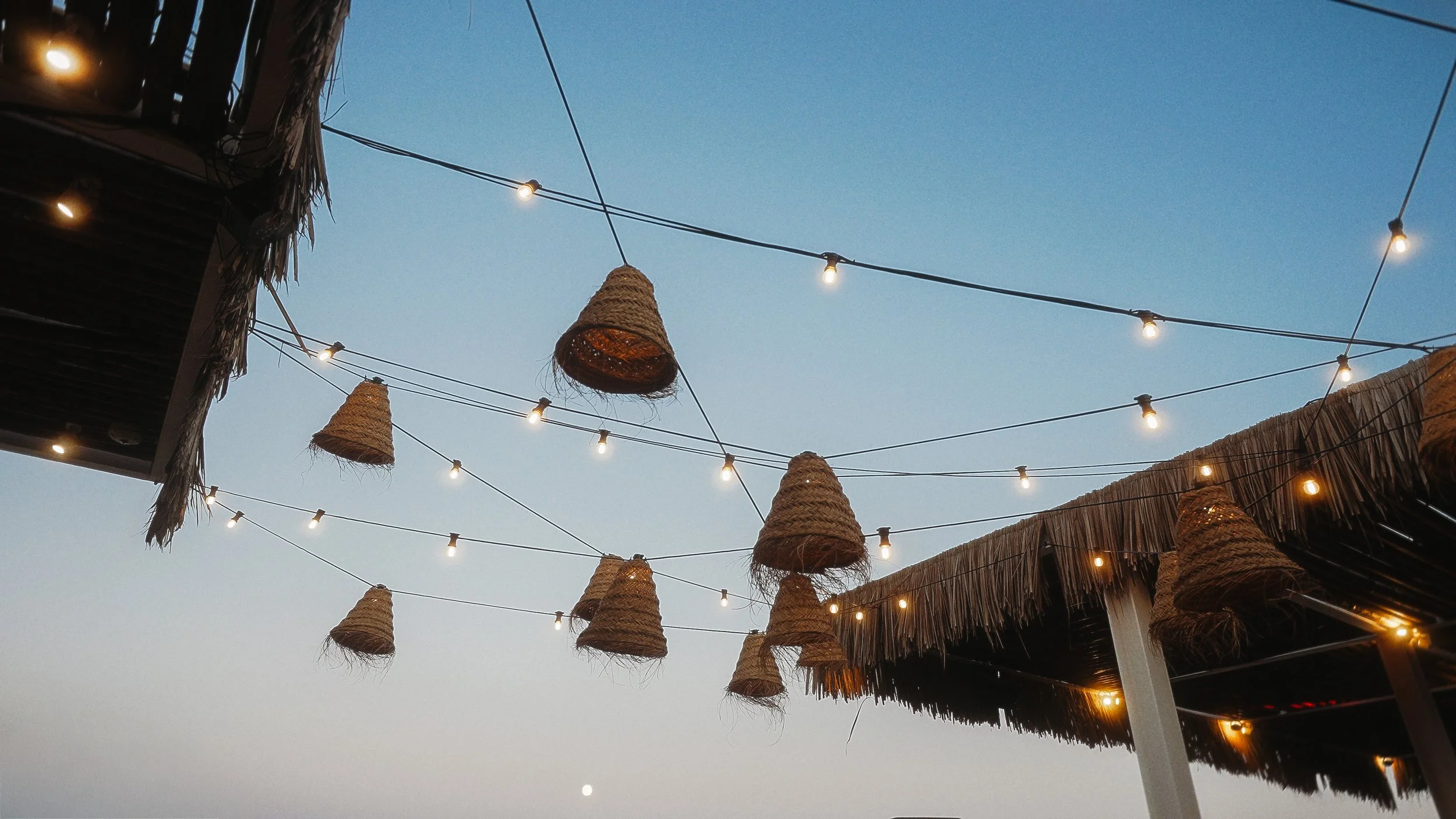 String lights and rattan pendants at dusk, wedding reception at Captain's Cabin Lady's Mile Beach Limassol, Red Lens Films