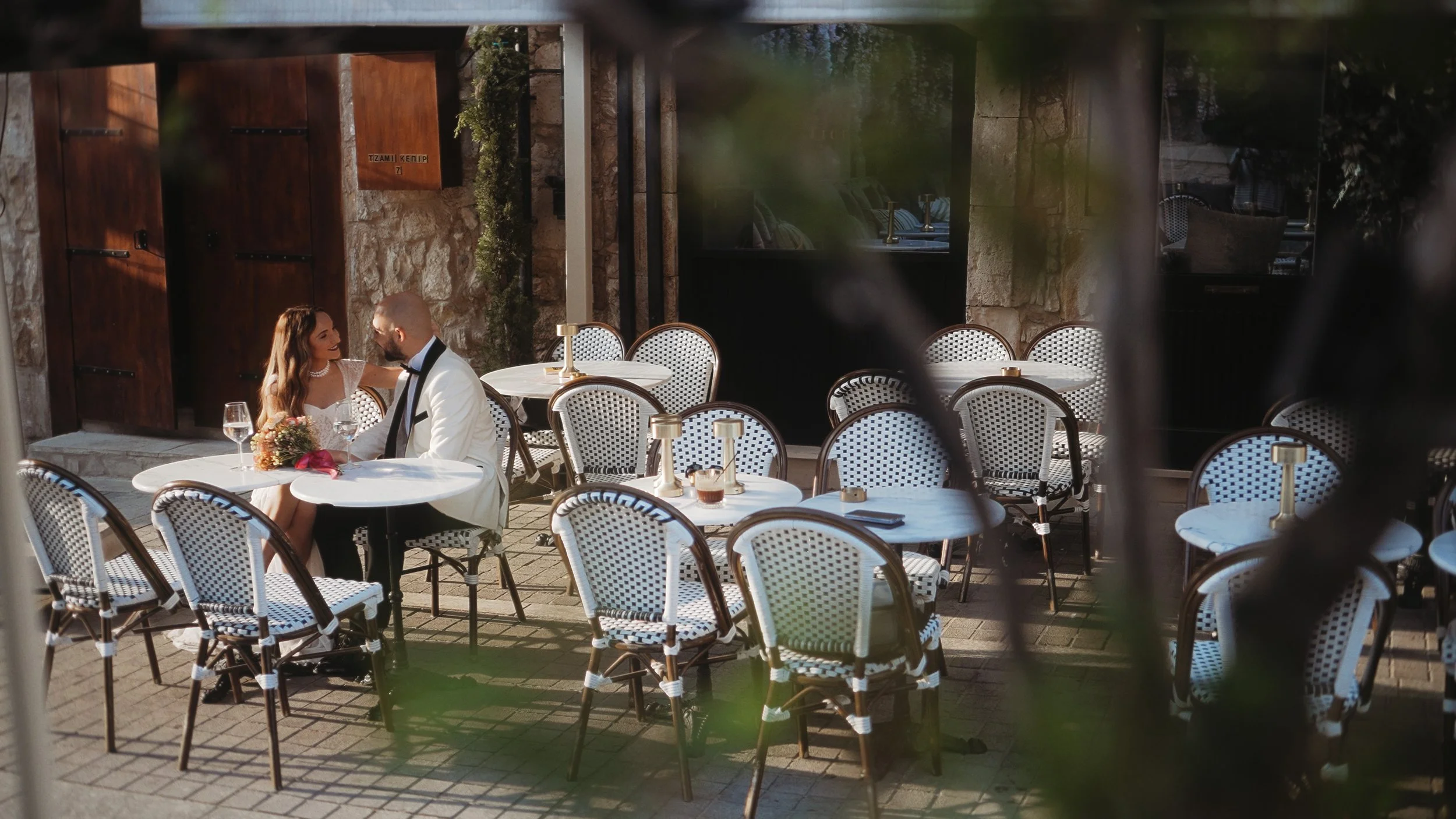 Couple sitting at outdoor café through foliage, Alice Coffee Limassol old town Cyprus, Red Lens Films