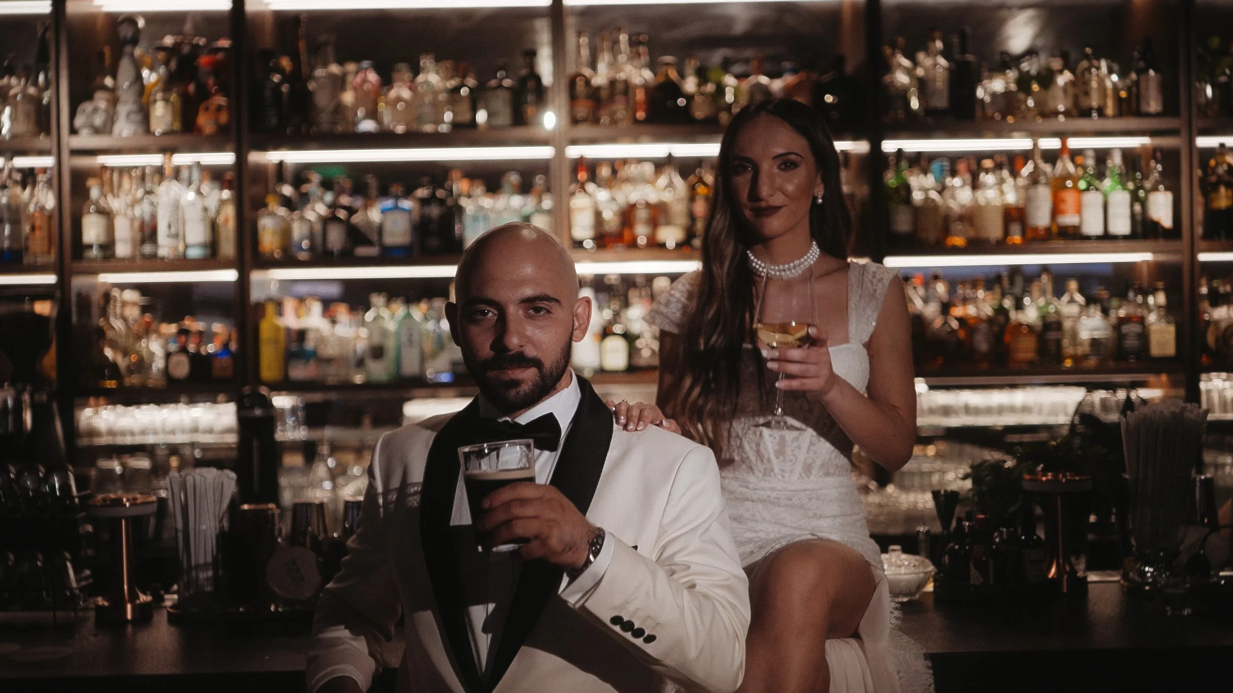 Couple posed at cocktail bar with drinks and backlit bottles, Tria Poulakia Limassol old town Cyprus, Red Lens Films