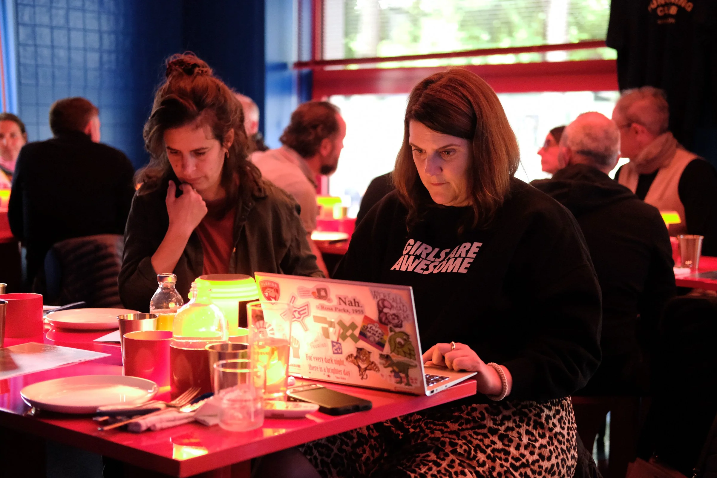 Menschen sitzen in einem Restaurant bei Kerzenlicht, essen und benutzen Laptops.