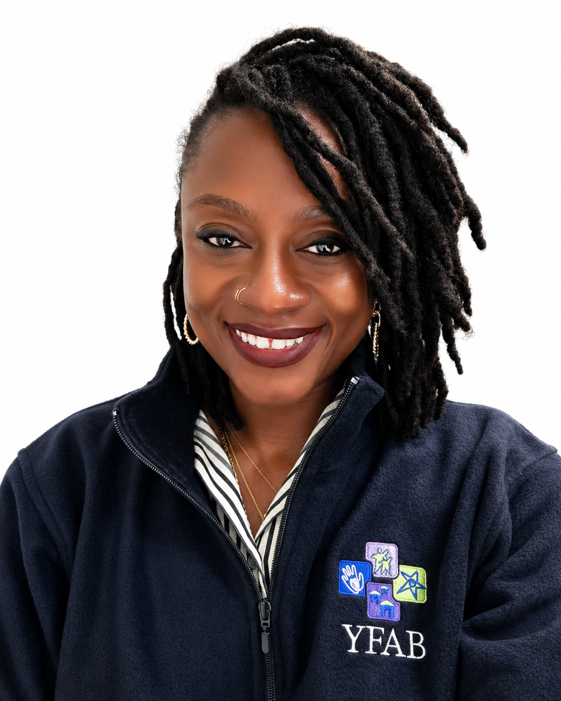 Smiling woman with dark skin, dreadlocks, wearing a navy jacket with YFAB logo, gold hoop earrings, and a nose ring, against a white background.