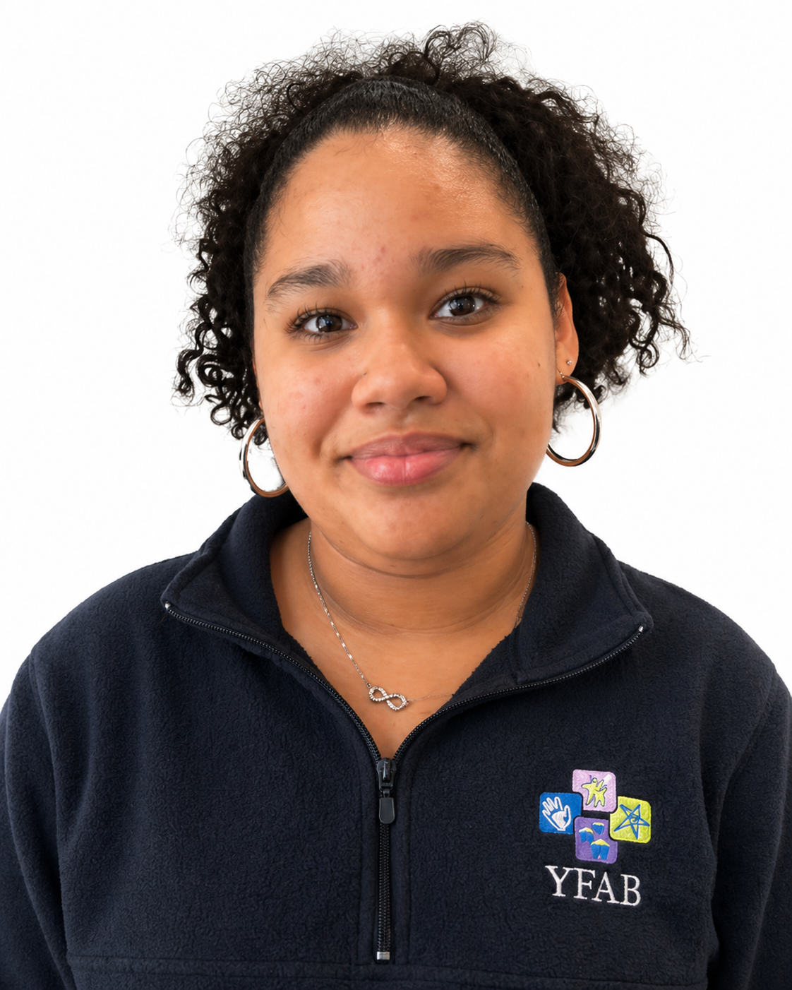 A young girl with curly hair, wearing a dark navy jacket with the YFAB logo, silver hoop earrings, and a silver necklace with a loop pendant, smiling at the camera against a white background.