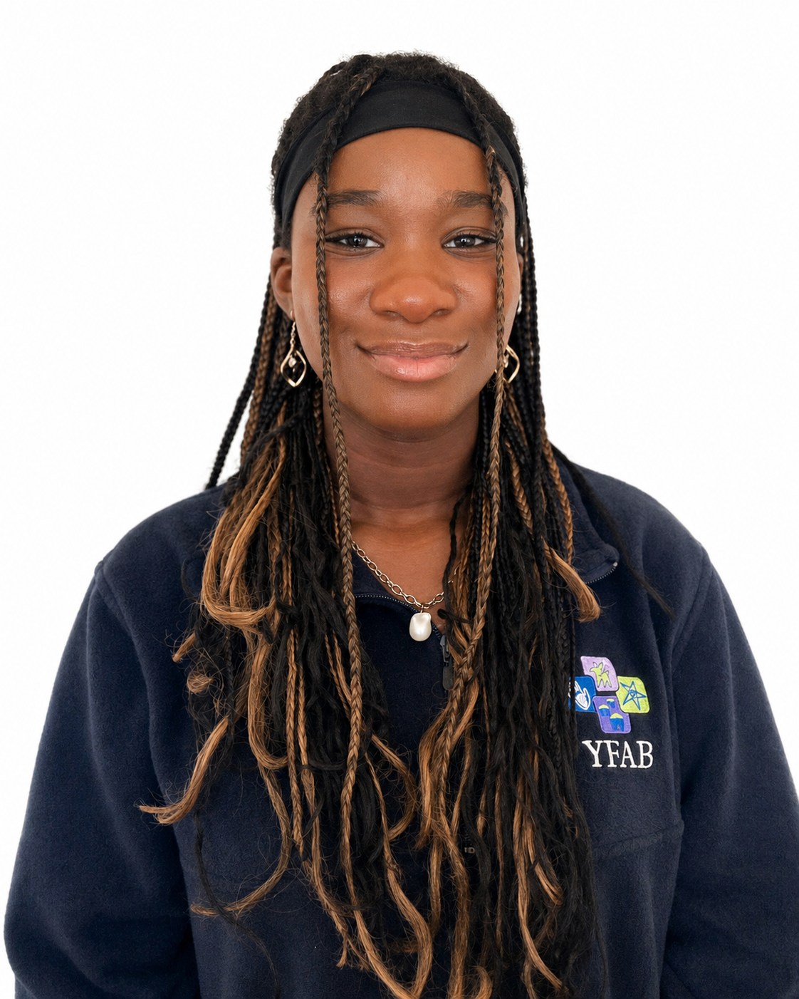 Front-facing portrait of a woman with medium-dark skin and long braided hair, wearing a black headband, earrings, a necklace with a pearl, and a navy zip-up jacket with colorful logo patches.