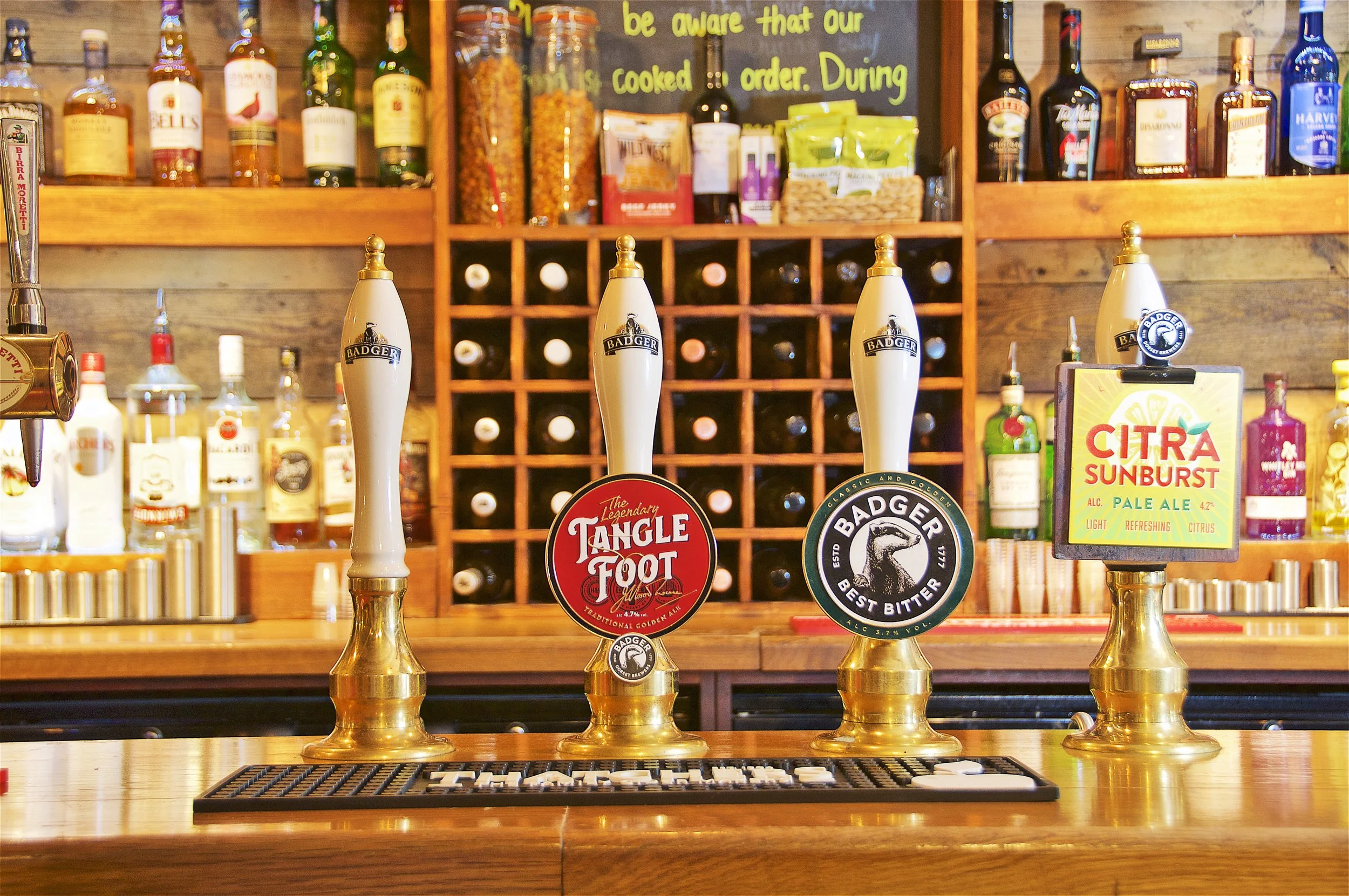 Bar with four beer taps and various liquor bottles on shelves in the background.