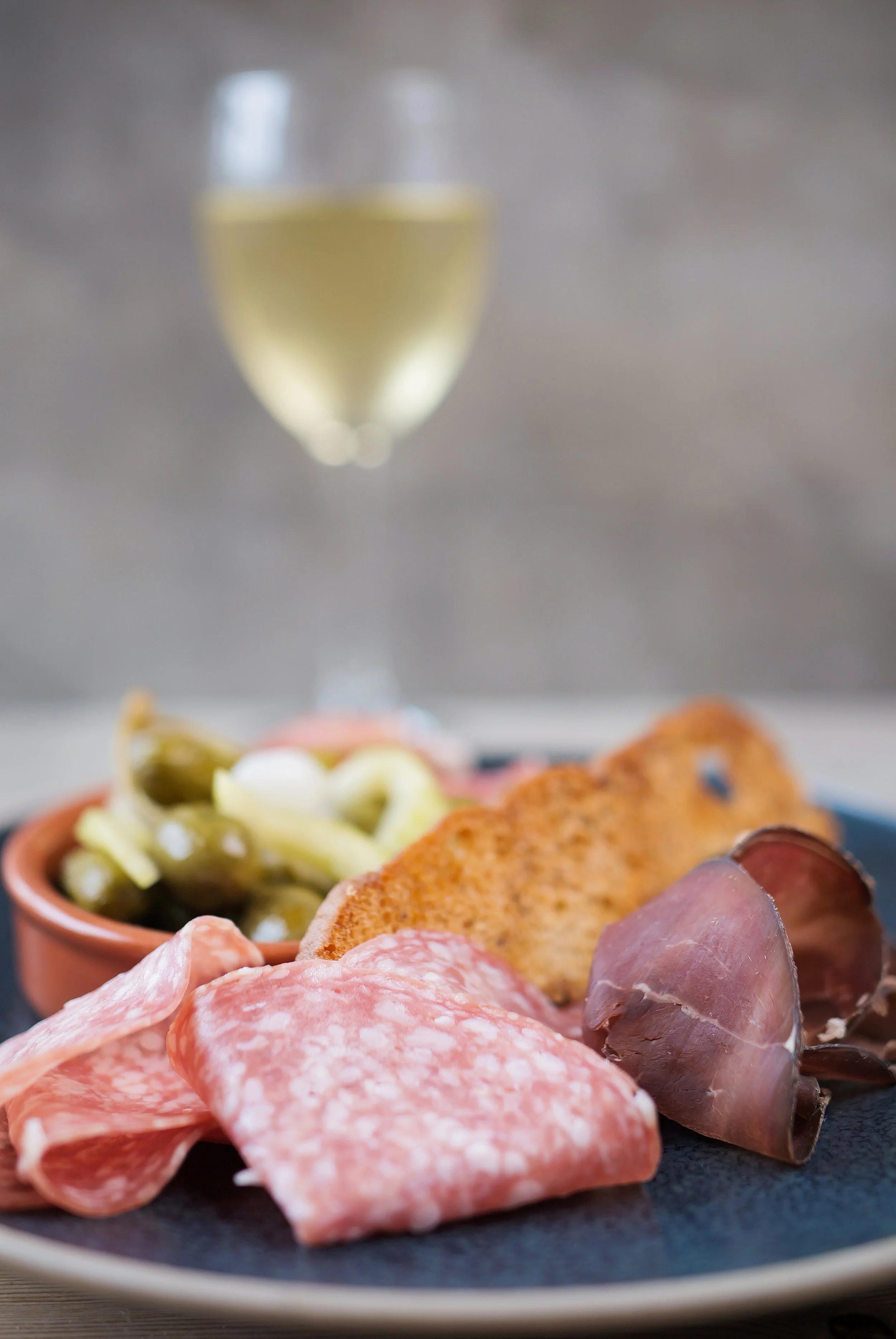 A charcuterie board with assorted cured meats, pickles, and crackers, accompanied by a glass of white wine.