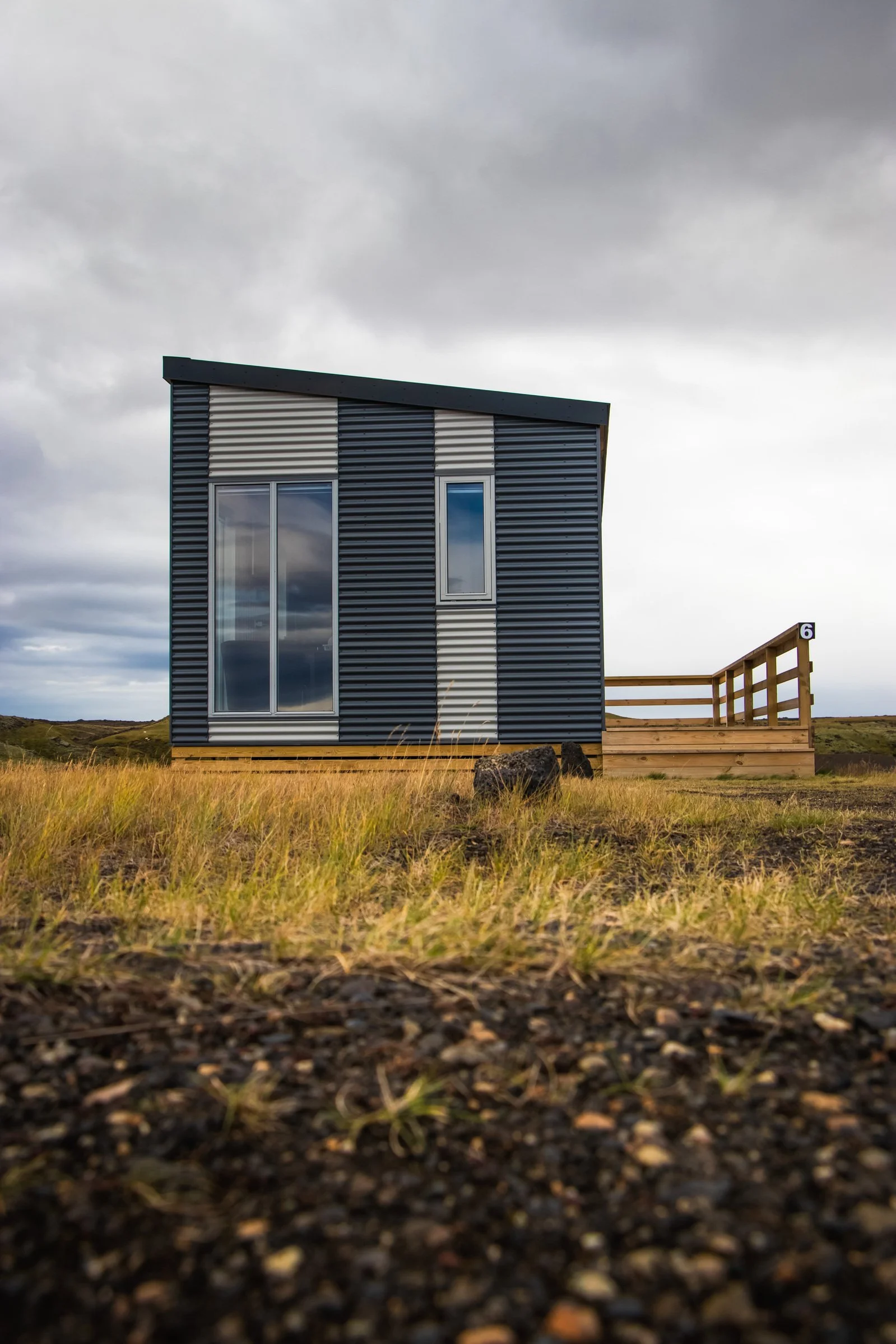Modern house with metal siding and large windows, situated on a grassy field under a cloudy sky.