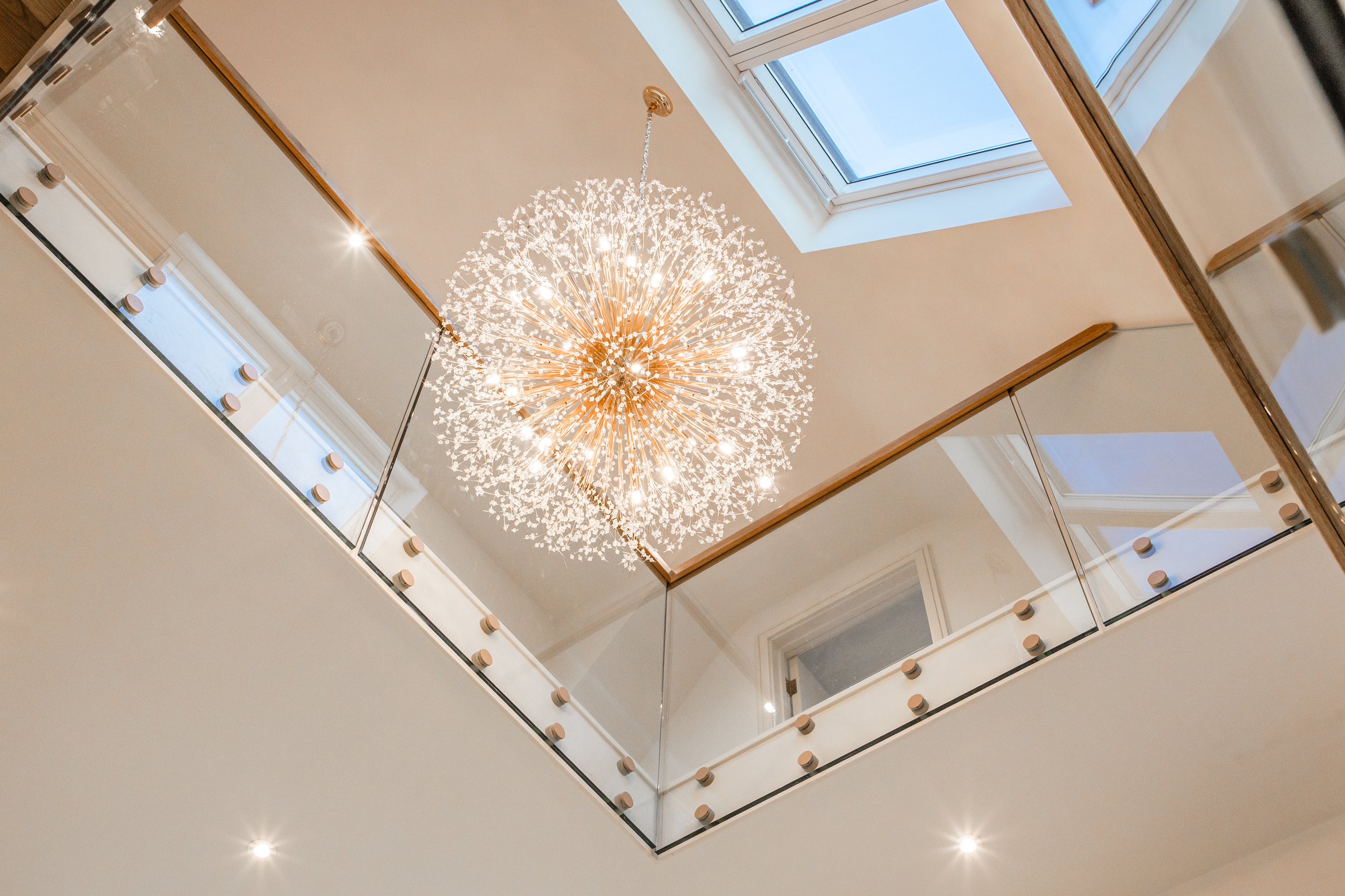 A chandelier hanging from a white ceiling with skylight windows, seen from the bottom looking up in an interior space.
