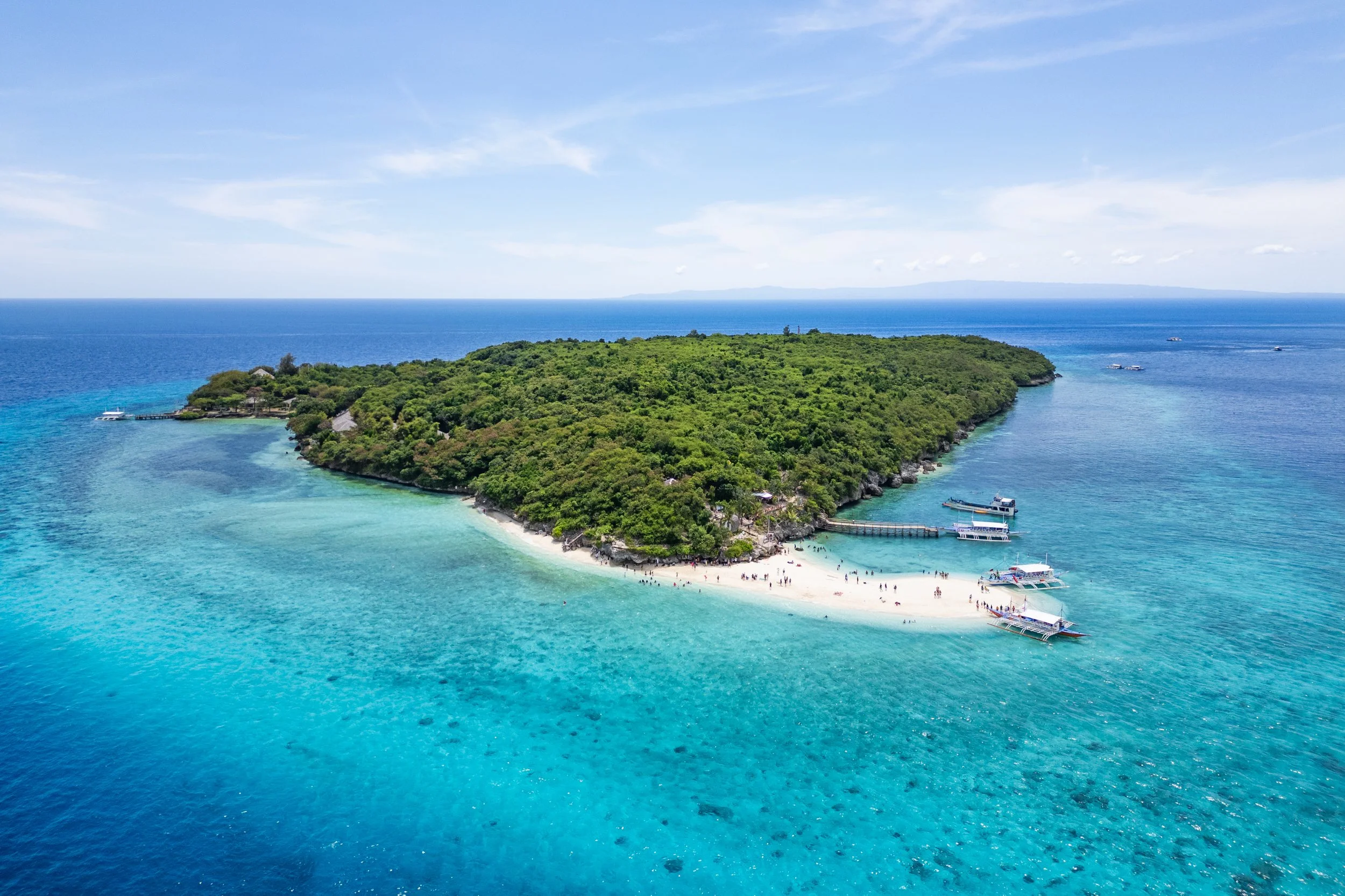 Aerial view of a tropical island with lush green vegetation, white sandy beaches, and clear blue water with boats docked near the shore.